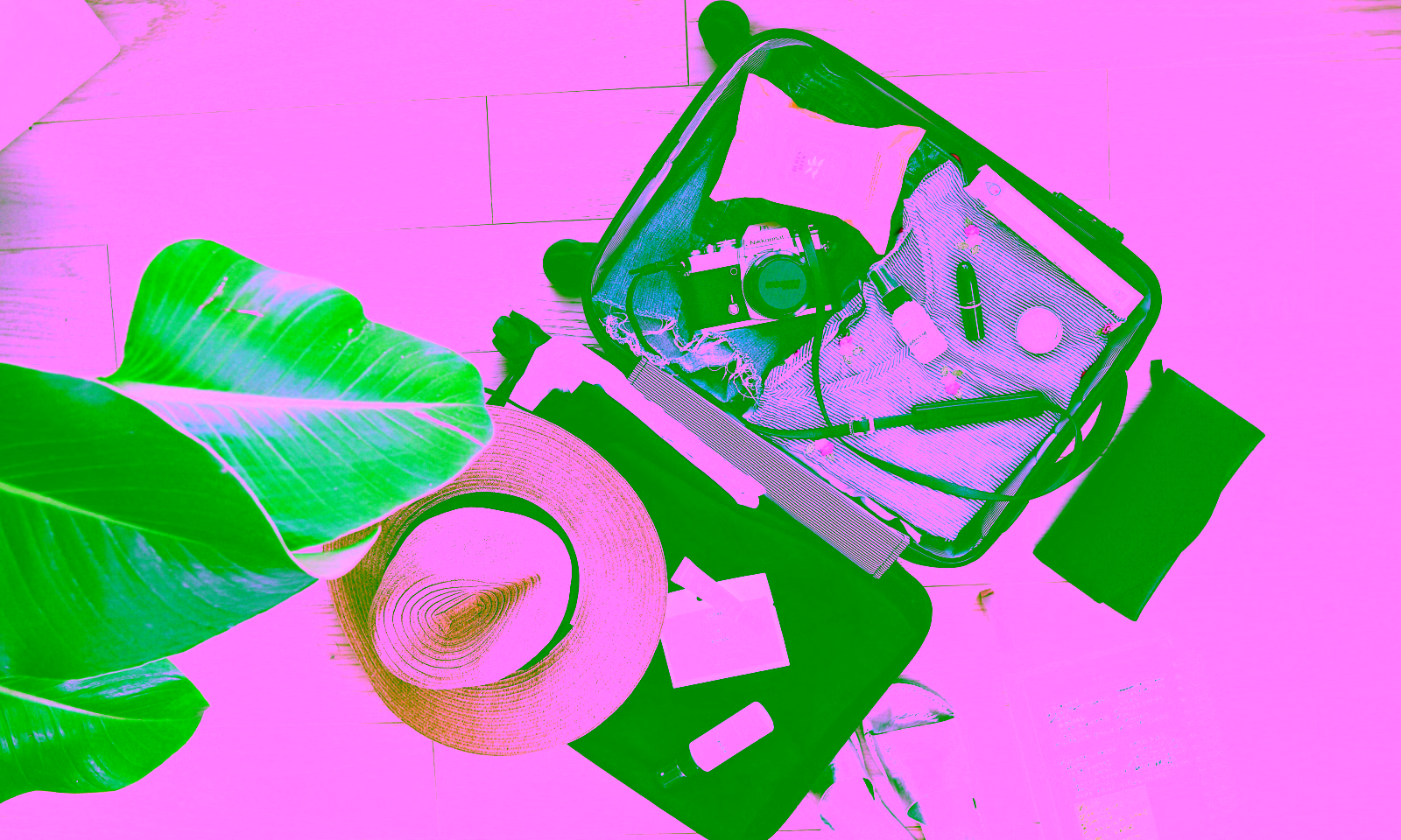 suit case open on the ground being packed with clothes, a camera, and a straw beach hat