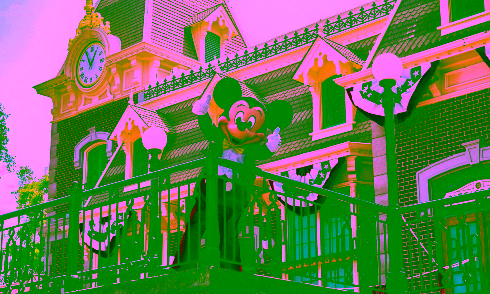 Mickey Mouse at Disneyland leaning over a railing from a walking giving a double thumbs up