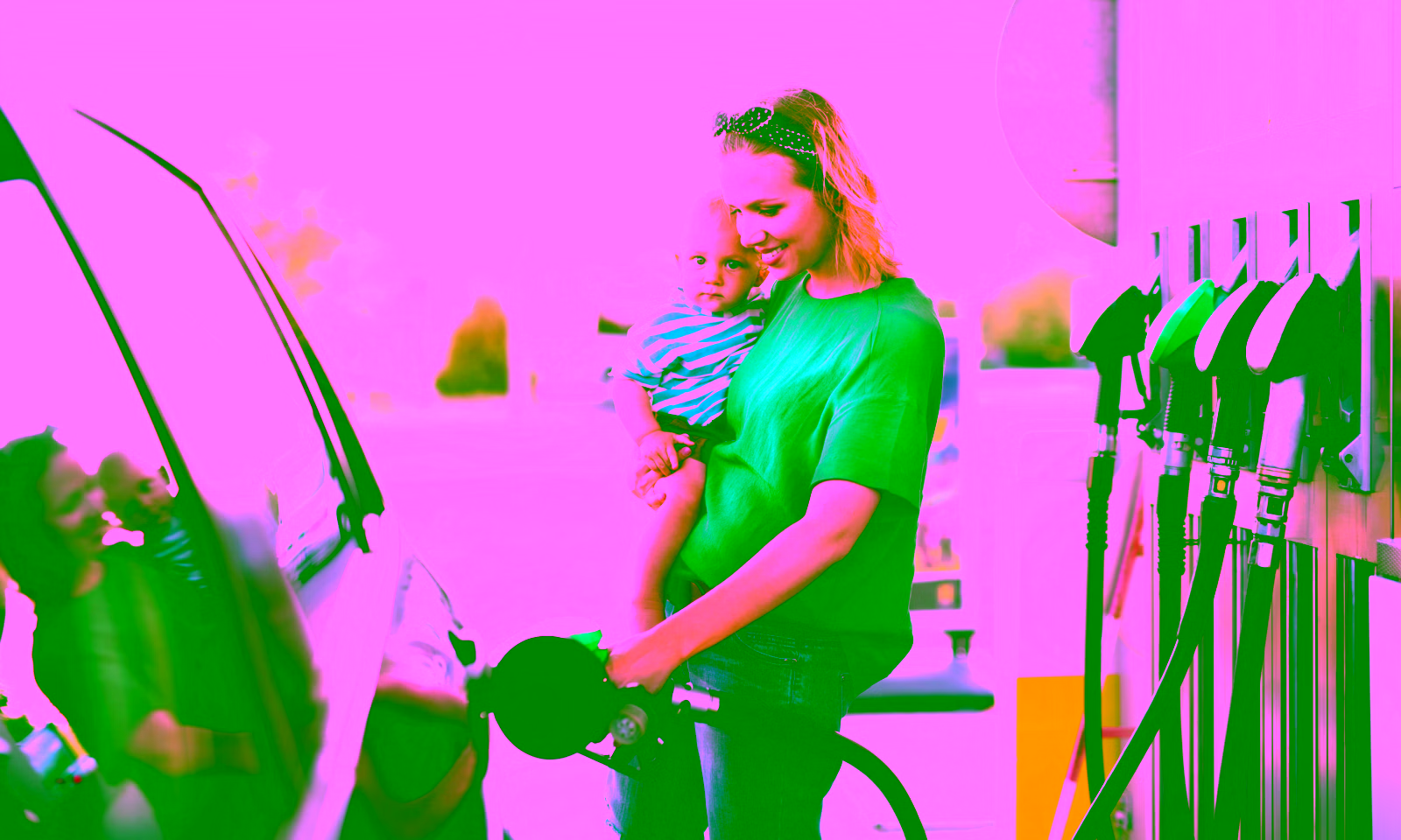woman hold a toddler while pumping gas at a gas station