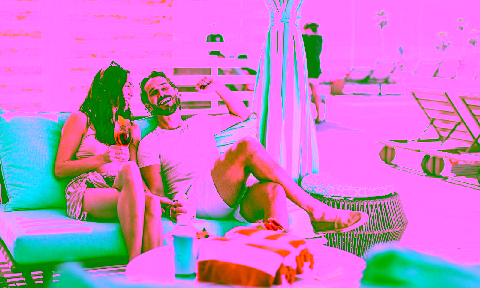 couple sitting in a cabana by a pool enjoying a drink while smiling