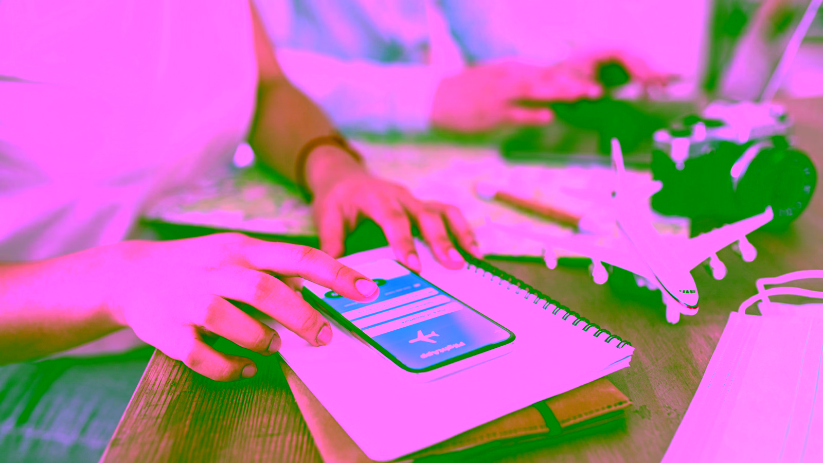 Person booking a flight on smartphone with travel items on desk