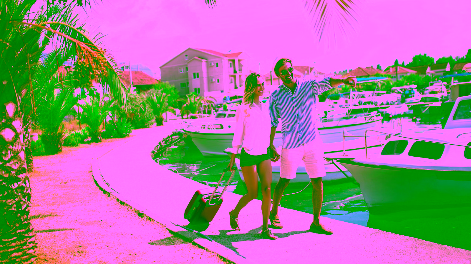 Couple traveling with suitcase near boats and palm trees