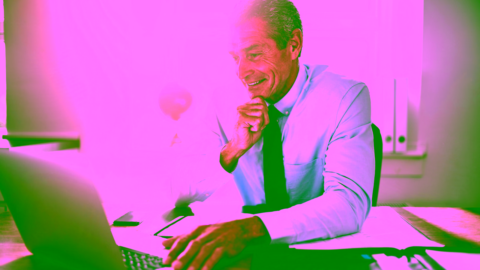 Man smiling while using a laptop at a desk