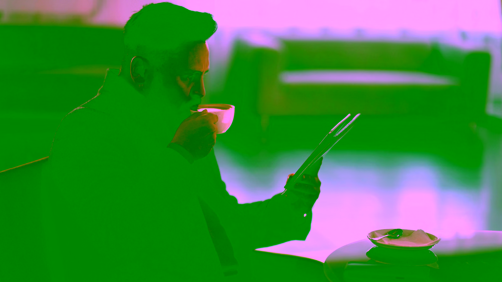 Man drinking coffee while reading on tablet