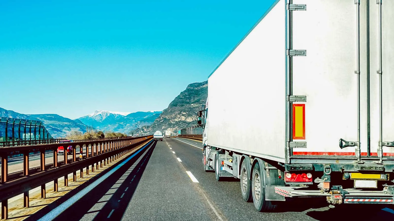 White semi trailer travelling a mountain highway beside a guardrail