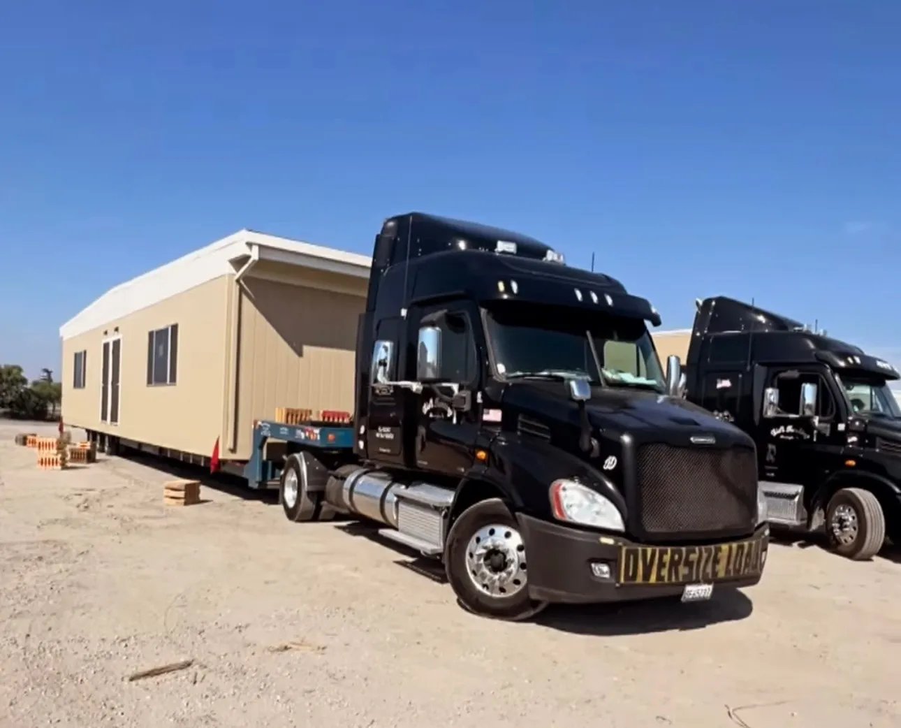 Black semi truck with oversize load banner hauling a modular building section