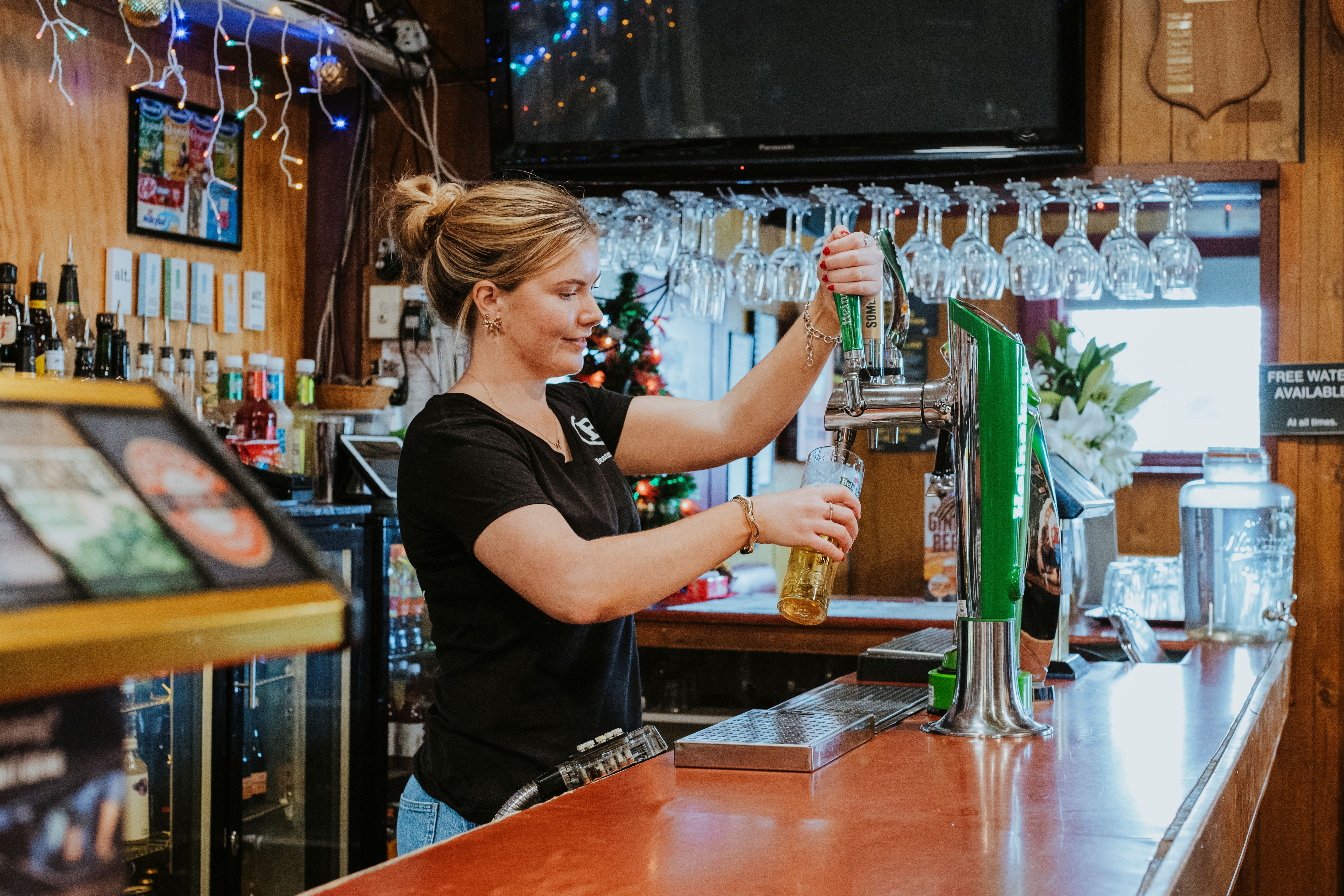 Bartender pouring beer from a tap into a glass behind a wooden bar counter.