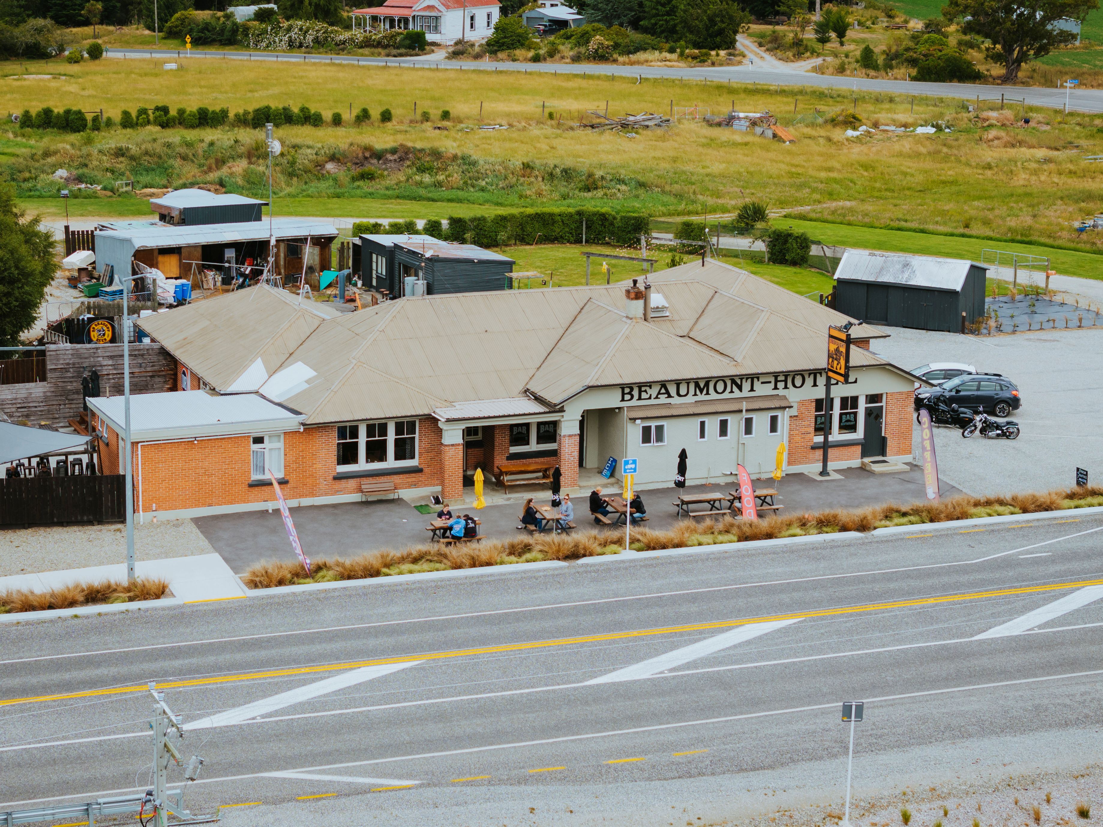 Exterior view of Beaumont Hotel with outdoor seating, people sitting at picnic tables, and motorcycles parked nearby.