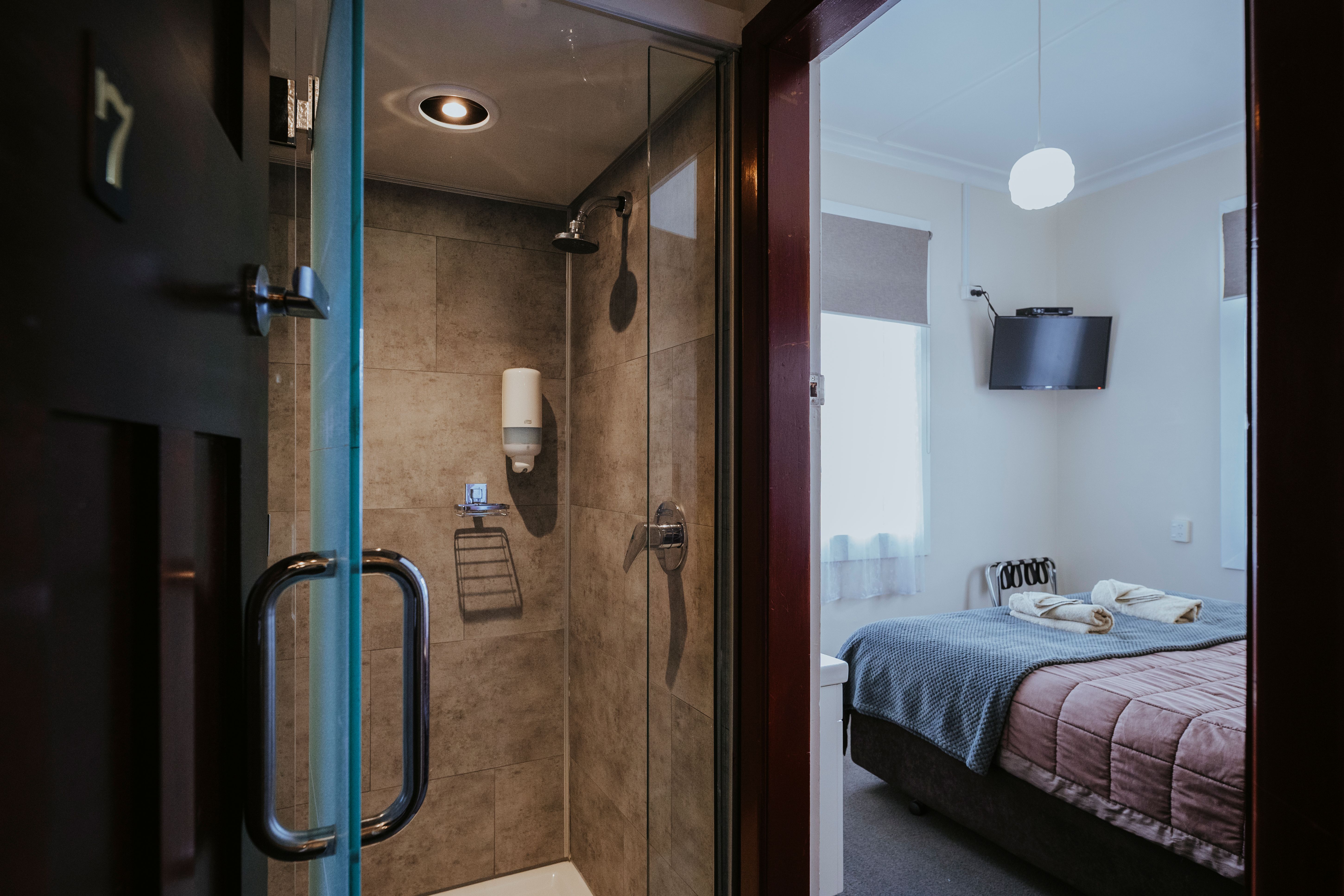 View of a hotel room showing a bed with blankets and towels, a mounted TV, and a glass door leading to a tiled shower.