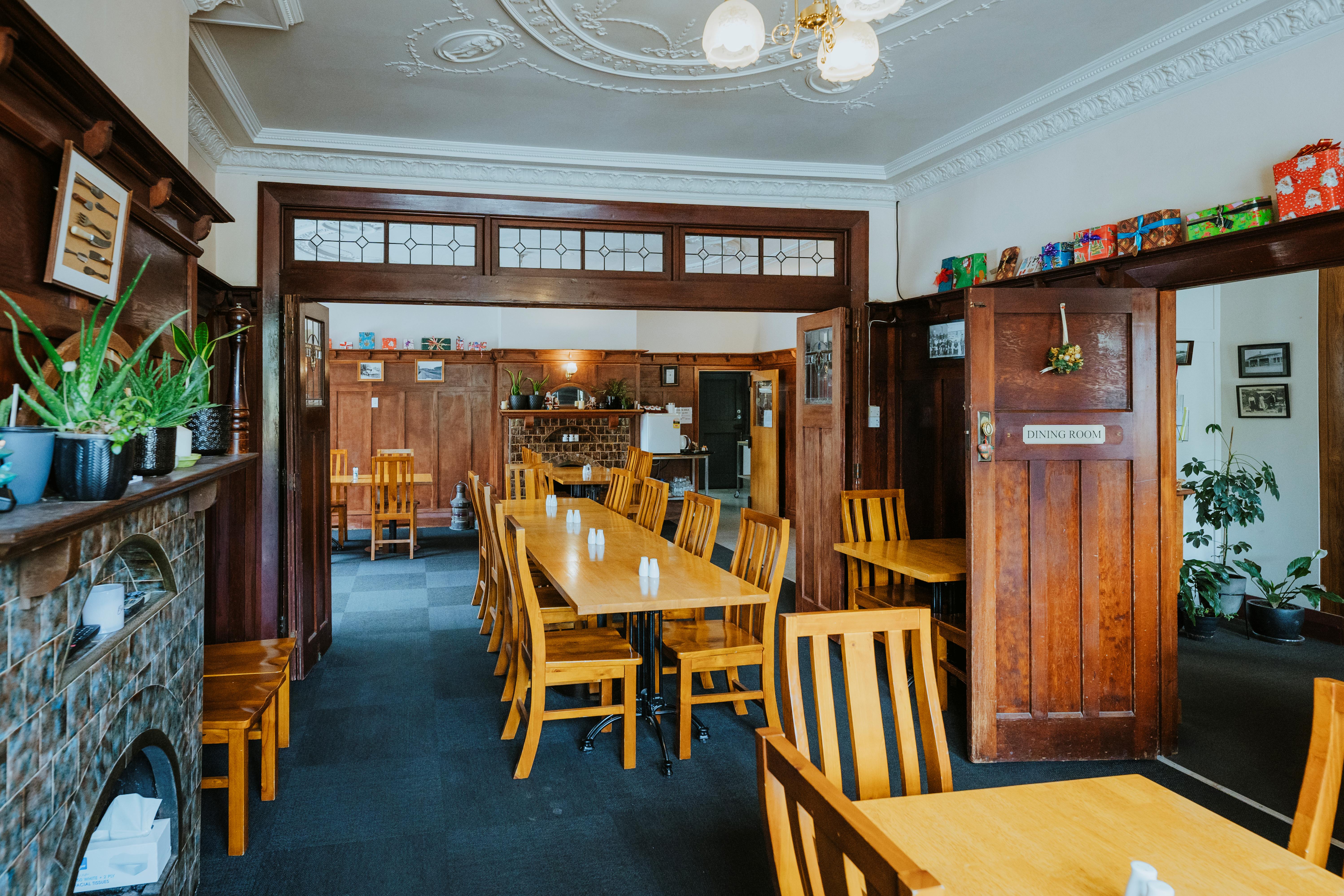 Dining room with wooden tables and chairs, dark carpet, wood-paneled walls, plants on mantel, and a door labeled 'DINING ROOM'.