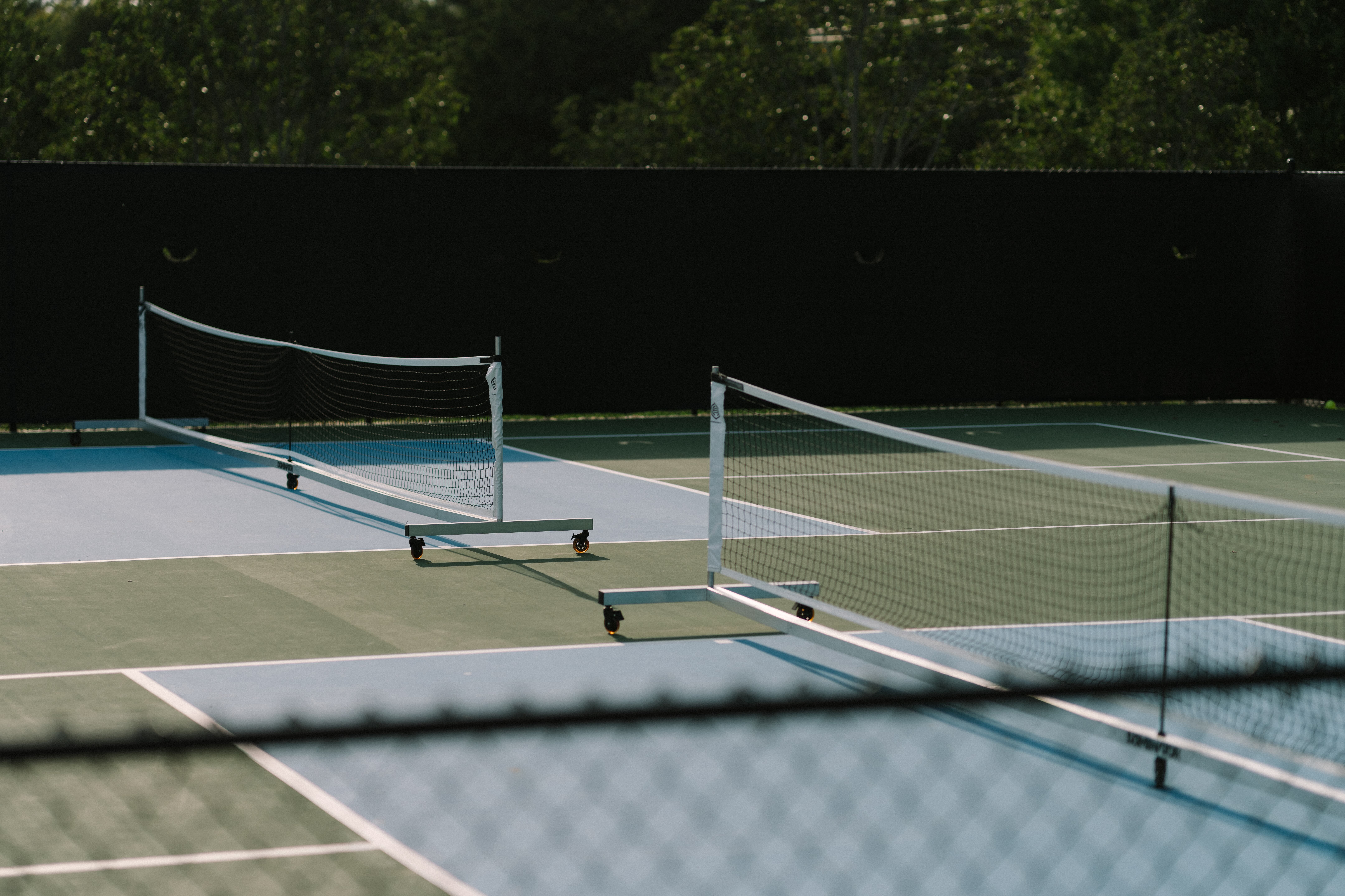 Two golfers on a putting green, one putting while the other stands holding a golf club, with a golf ball near the hole and flags on the green.