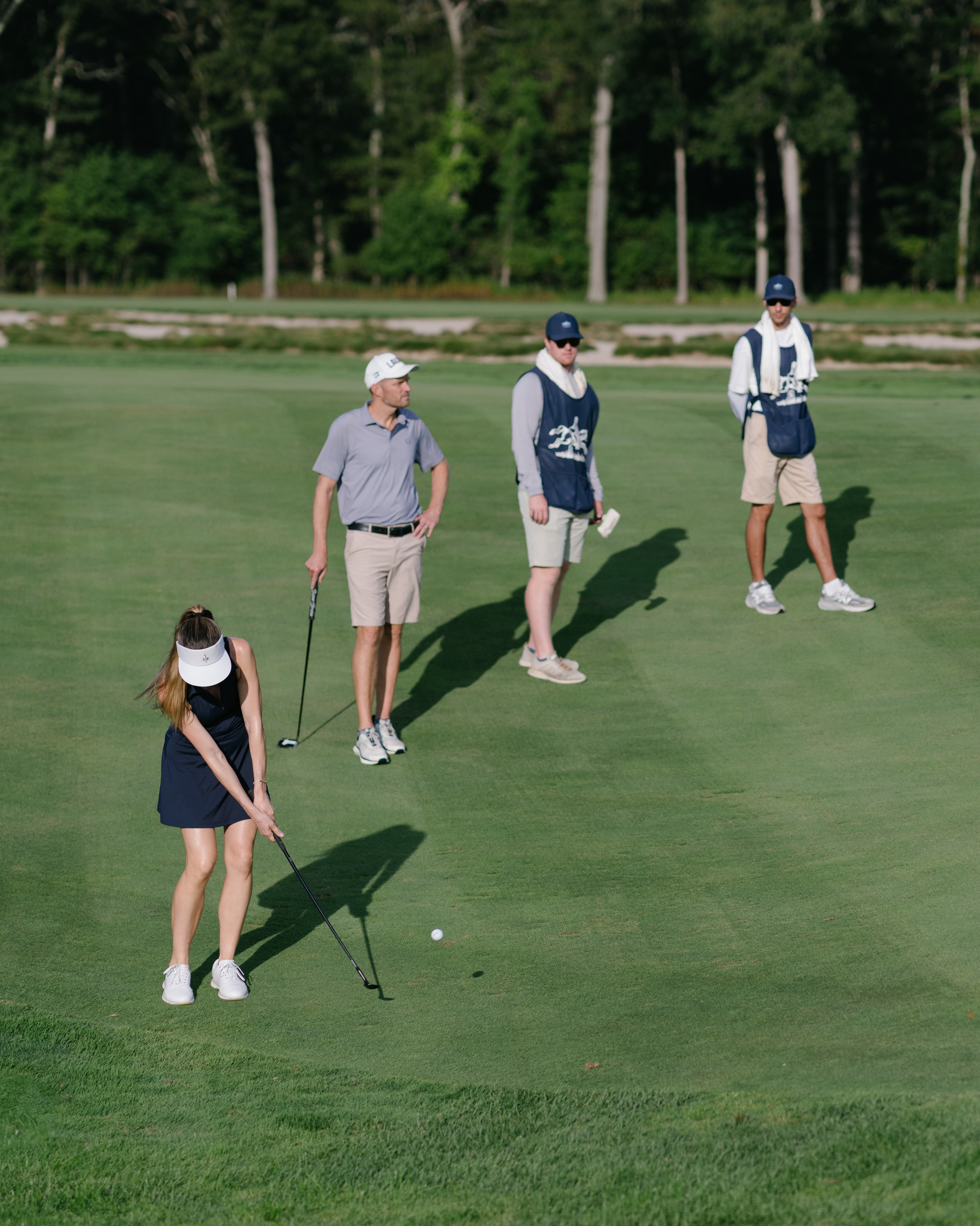 Female golfer putting on a green with two male golfers and two caddies watching nearby.
