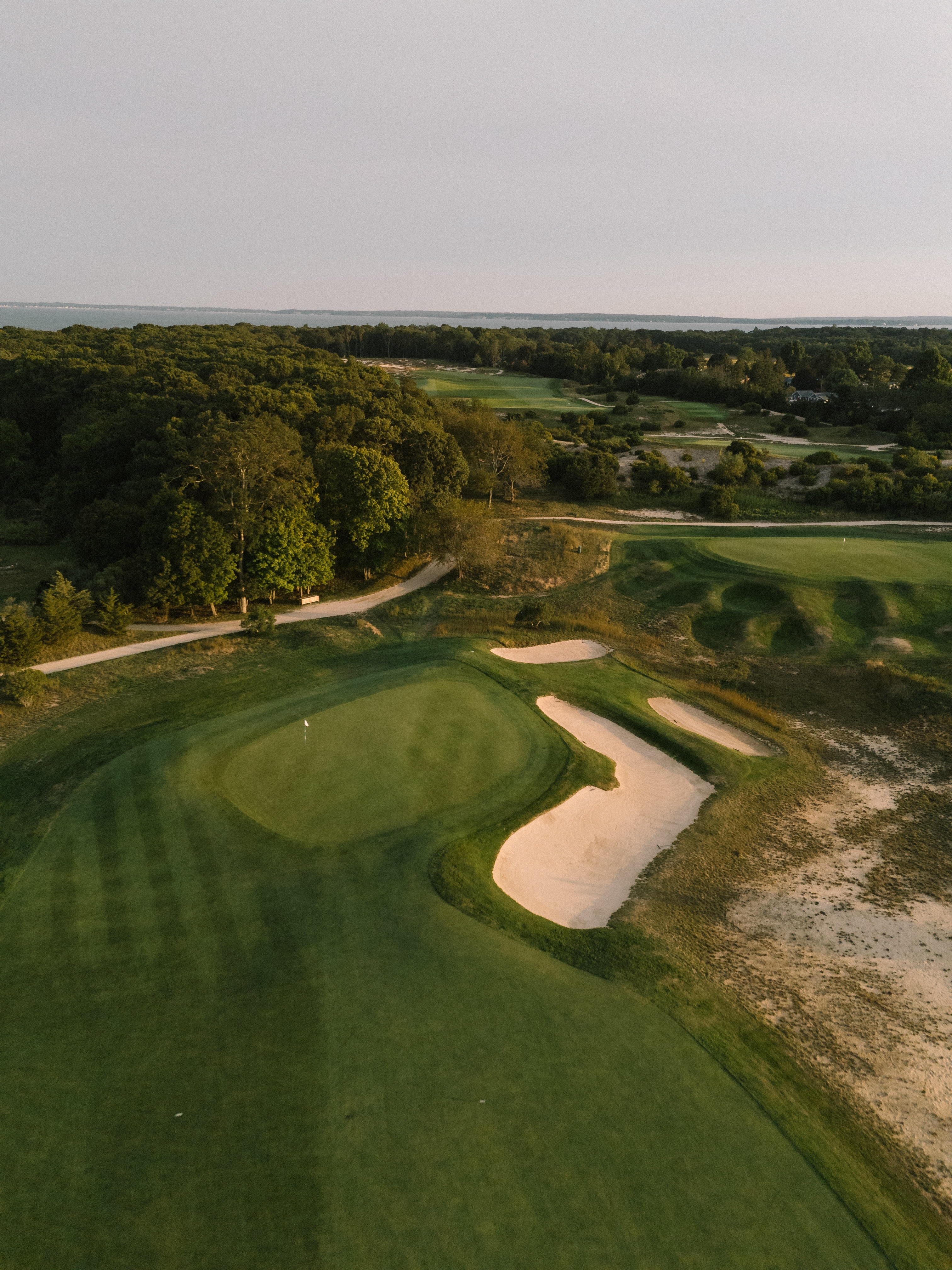 Aerial view of Laurel Links Country Club with several sand bunkers, green fairways, and surrounding trees under a clear sky.
