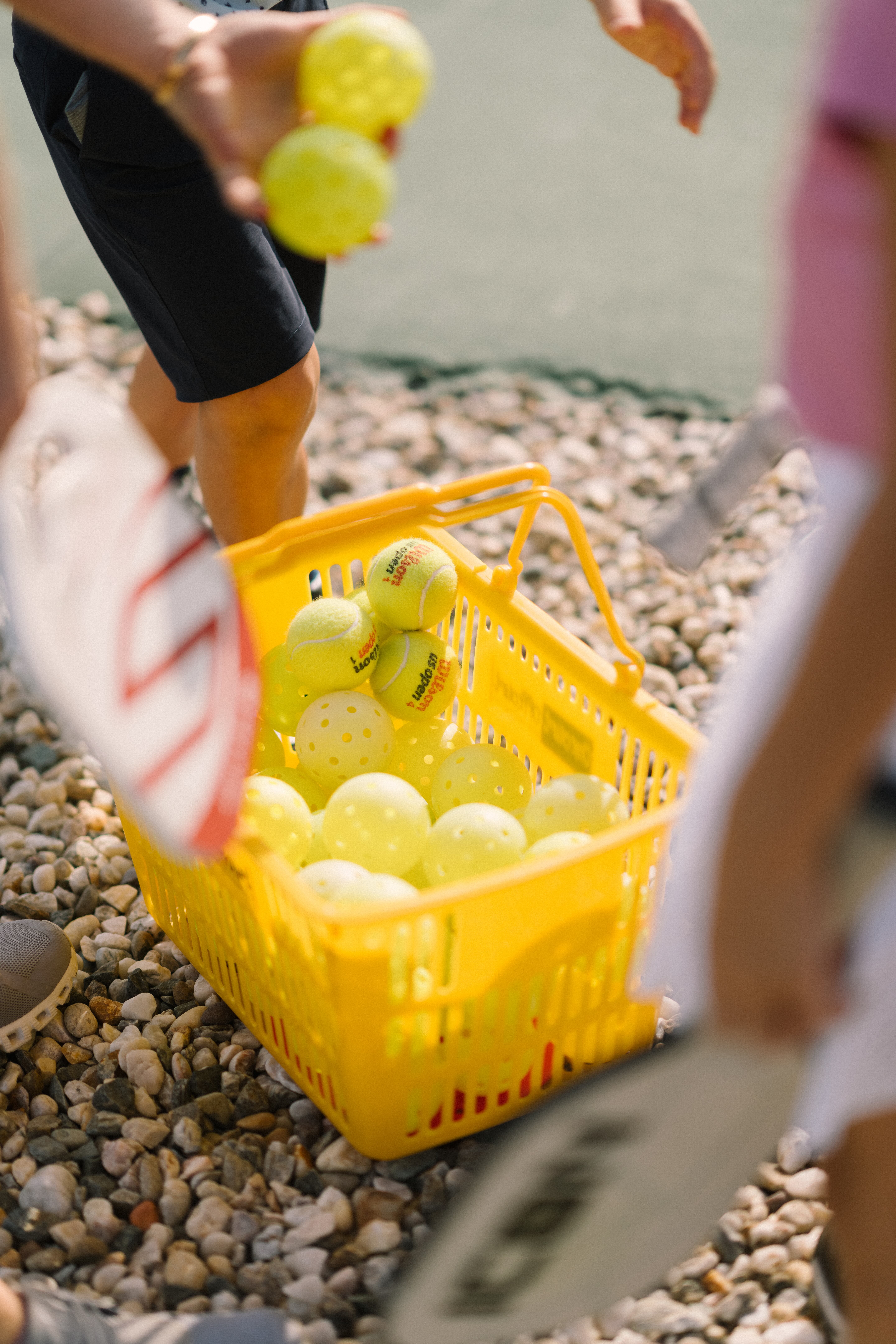 Three tennis rackets resting on a bench under a green and white striped canopy at a tennis court.