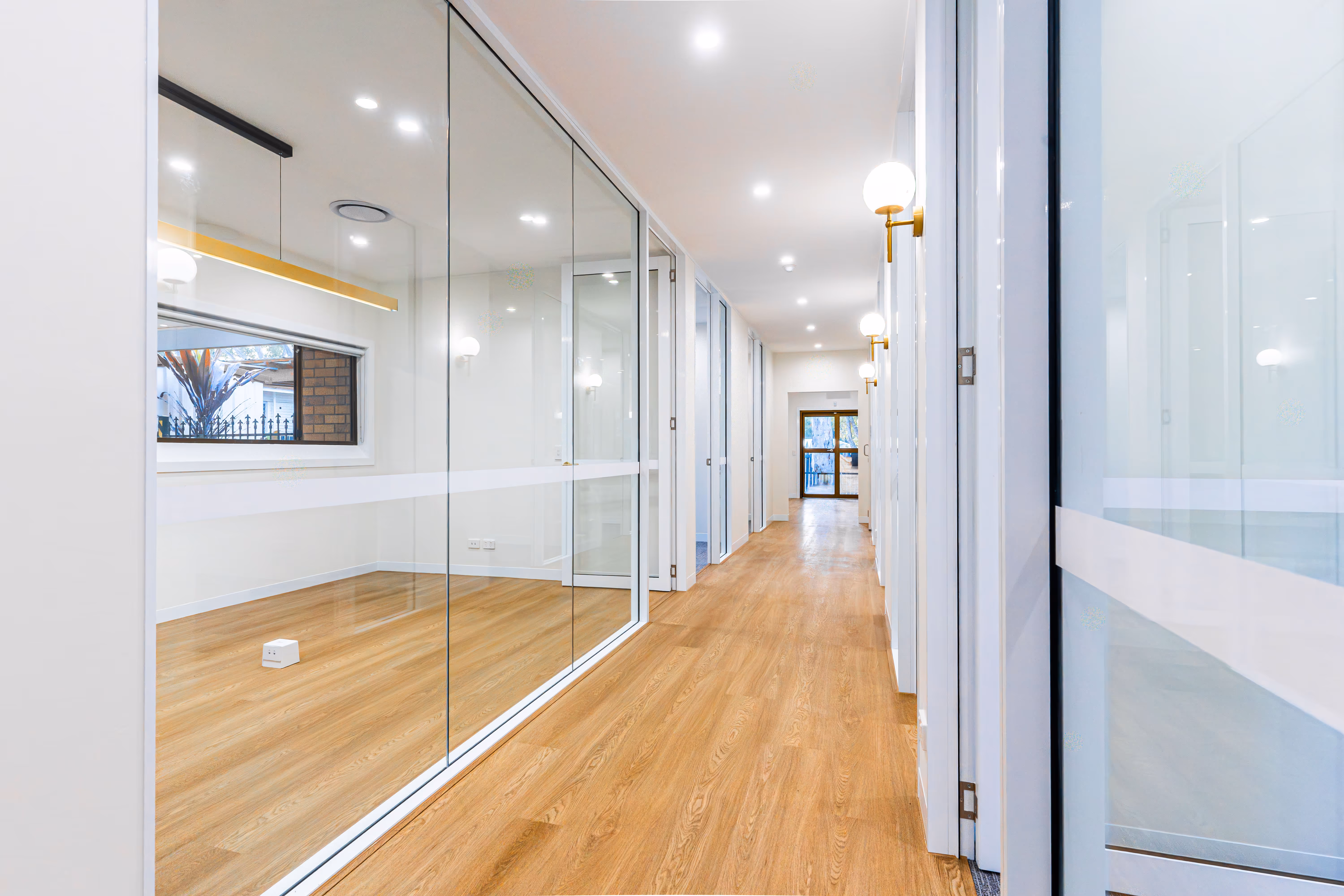 Bright, modern hallway with wooden flooring and glass office partitions on the left.