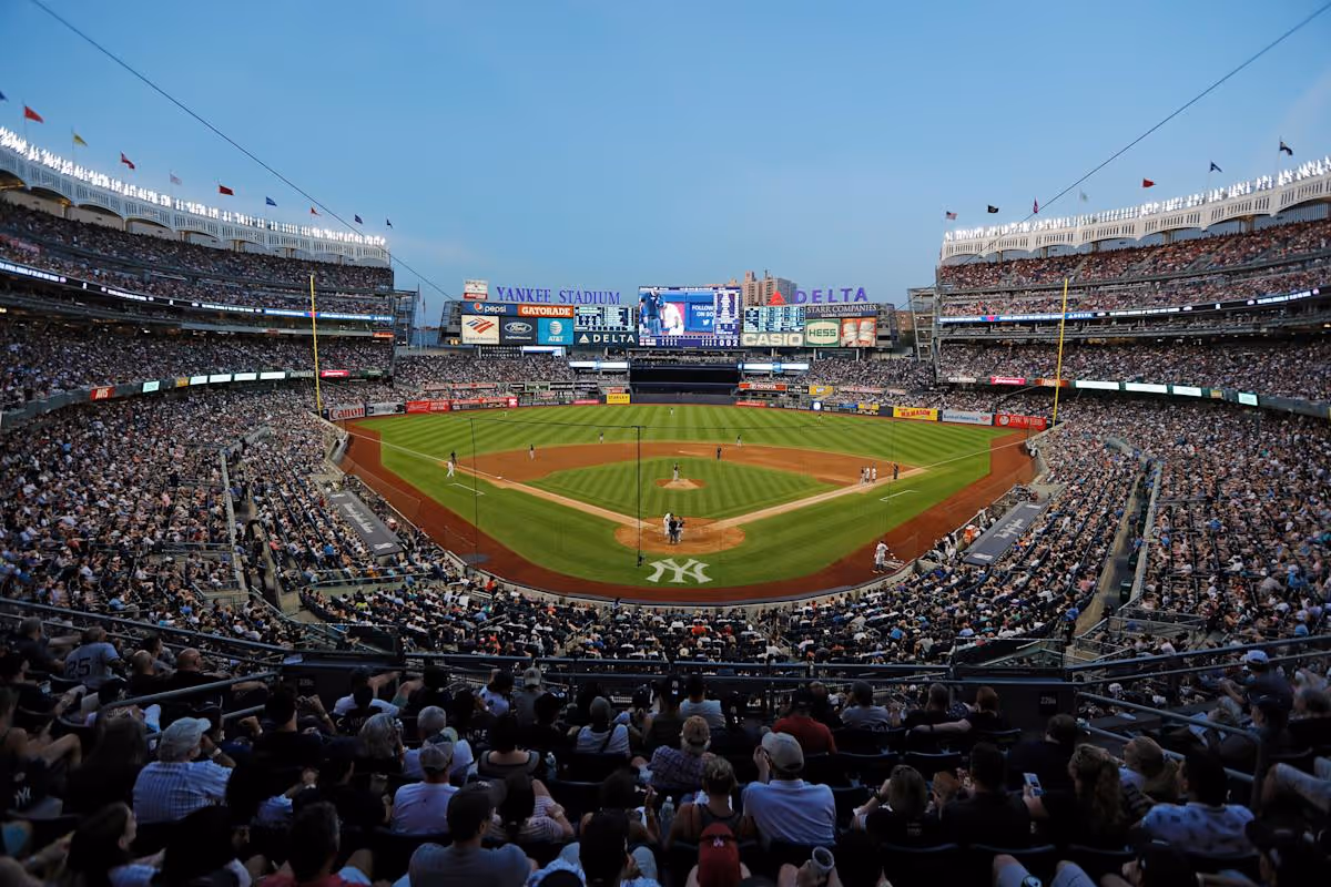 Wide view of Yankee Stadium filled with spectators during a baseball game at dusk.