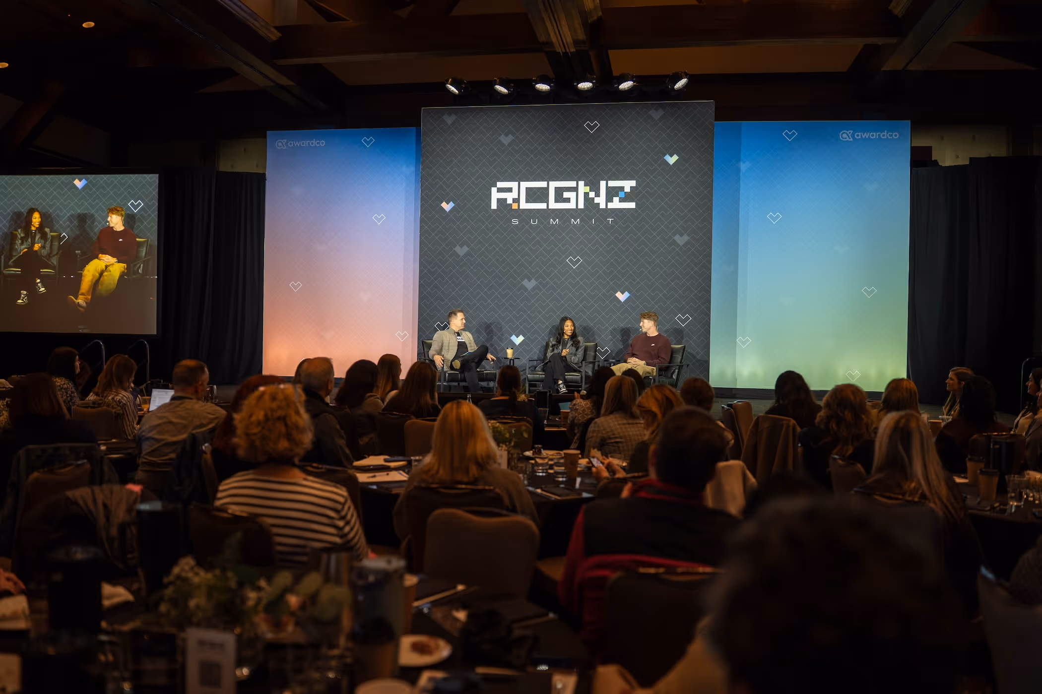 Panel discussion at the RCGNZ Summit with three speakers seated on stage and a large audience watching.