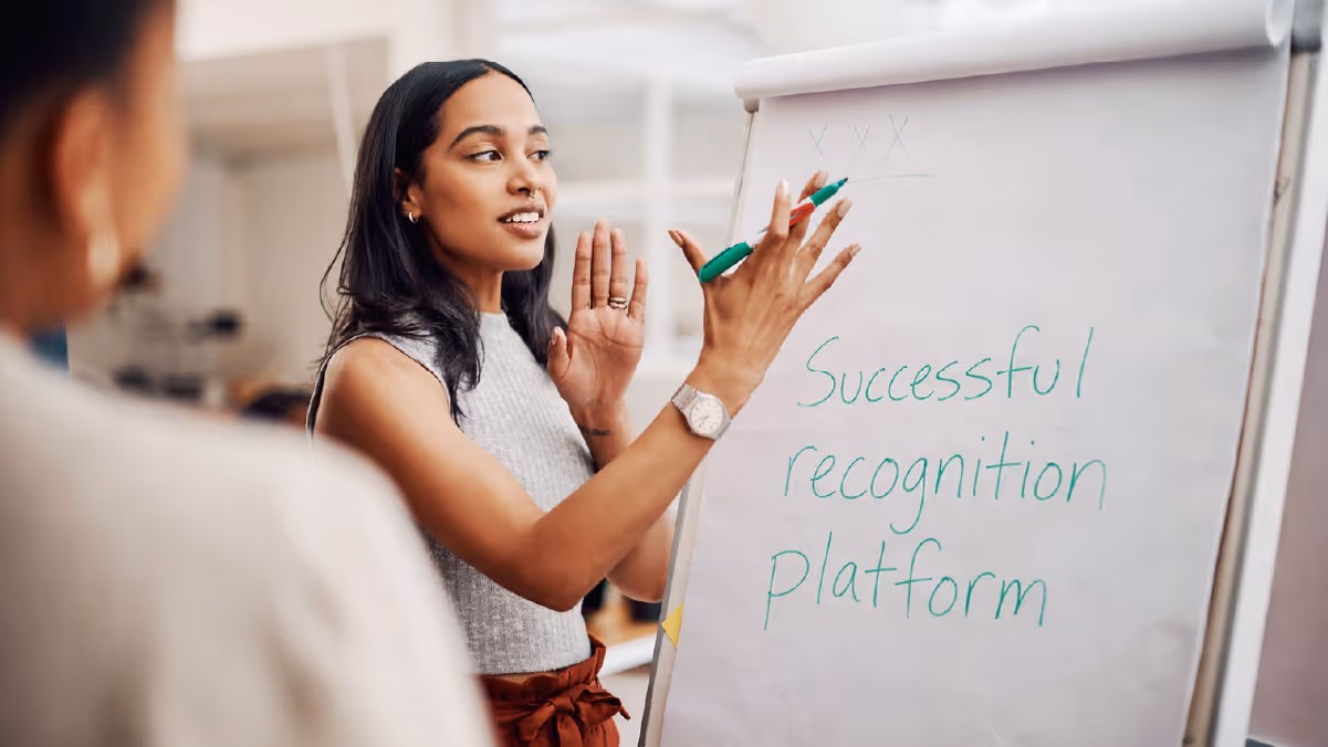 A woman presenting with a green marker in front of a flip chart with the words 'Successful recognition platform' written on it.