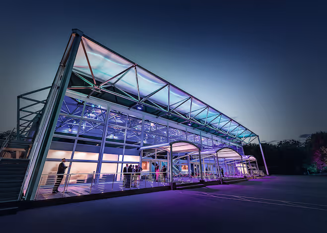 Modern glass and steel building illuminated with purple and blue lights at dusk.