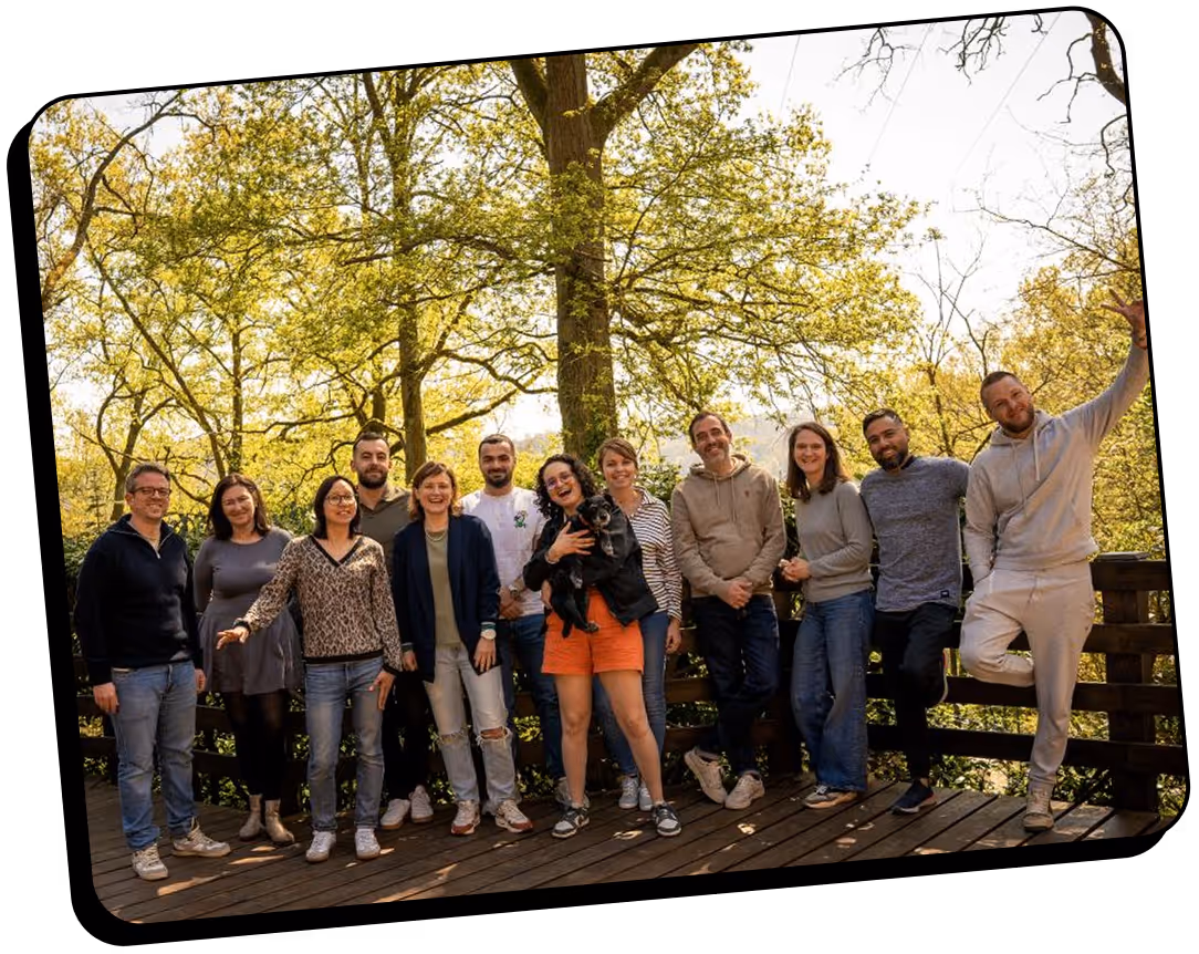 Un groupe hétéroclite de 14 personnes se tient sur une terrasse en bois entourée d'arbres verdoyants, souriant et posant pour une photo.