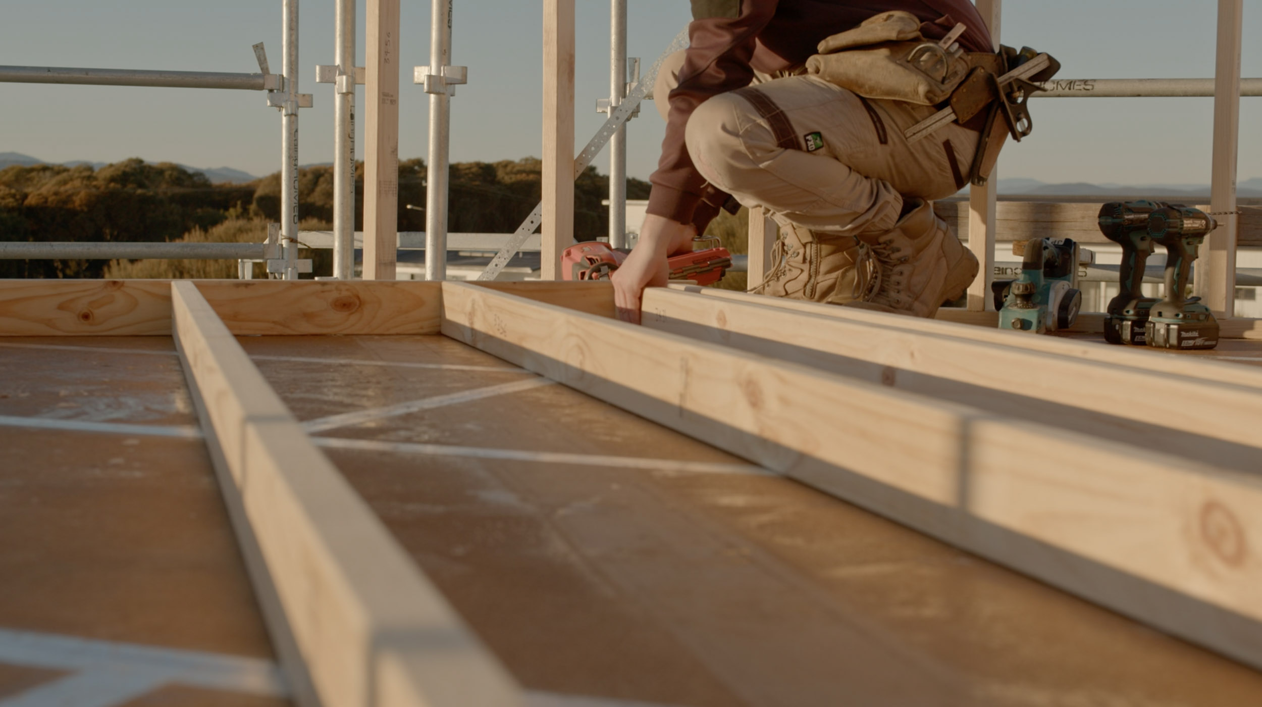 A person fitting some nails to a wooden house frame.