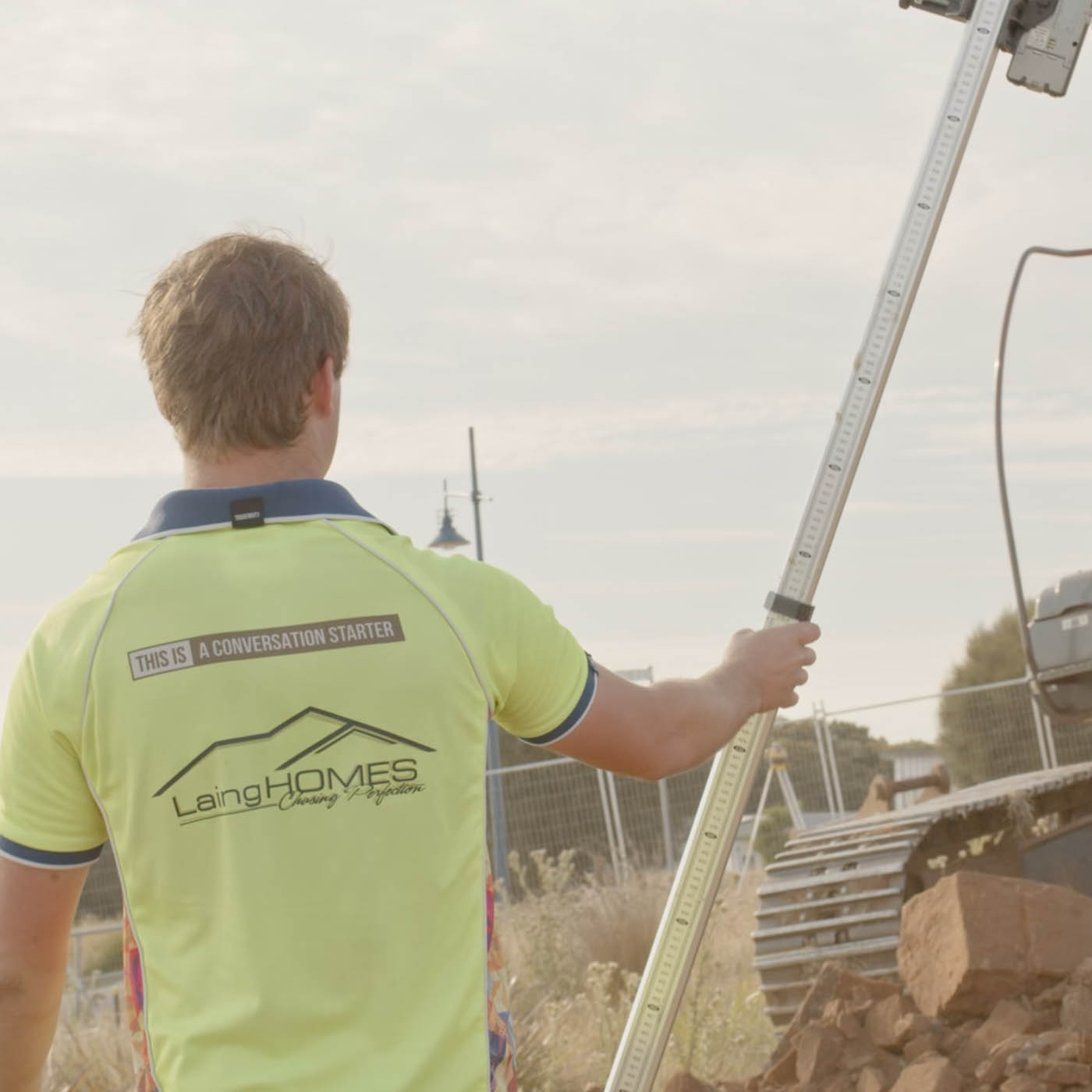 A person standing up holding a pole facing a orange excavator.