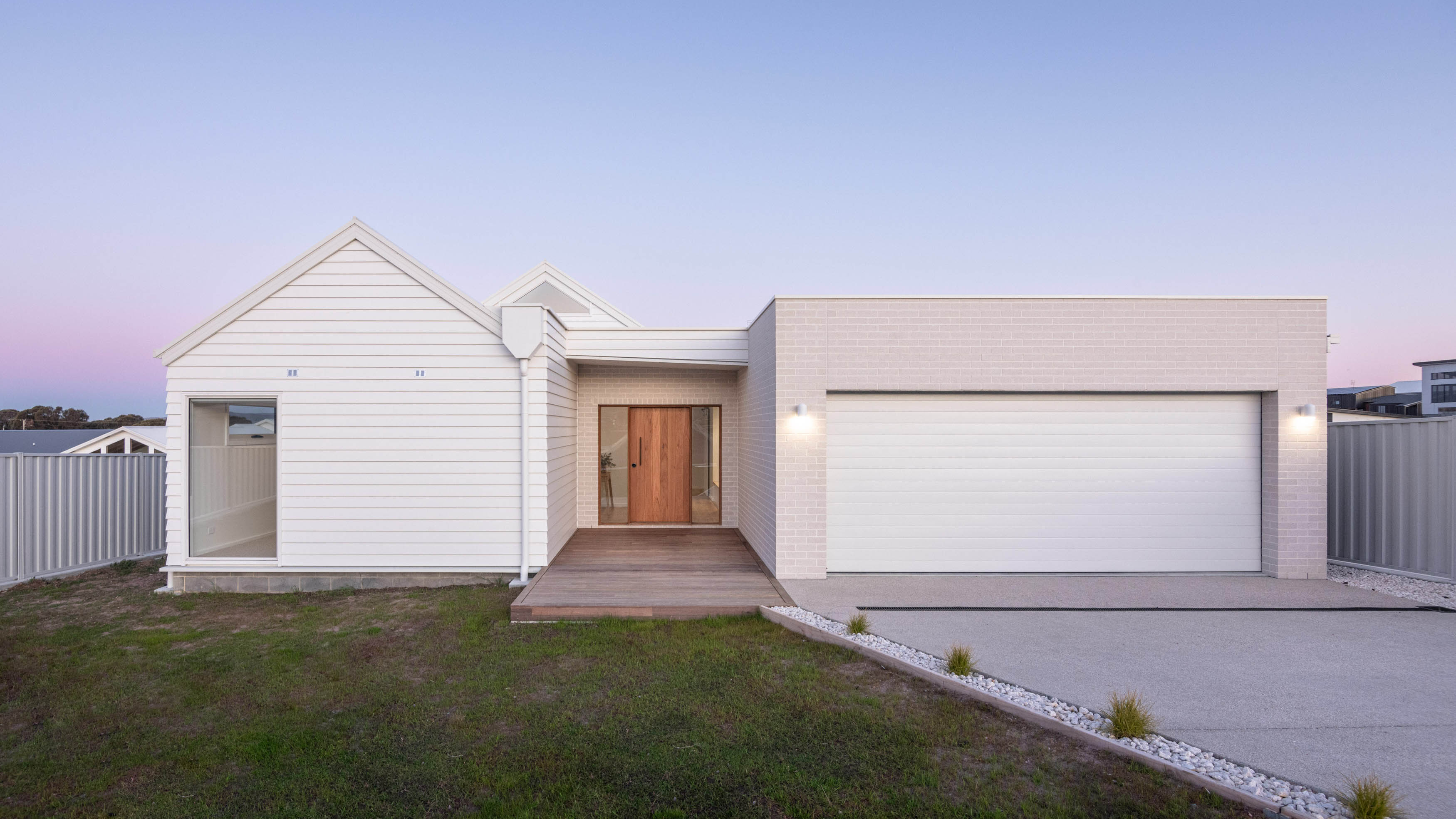 An image of a white and sand coloured house with outside lights on during a sunset.