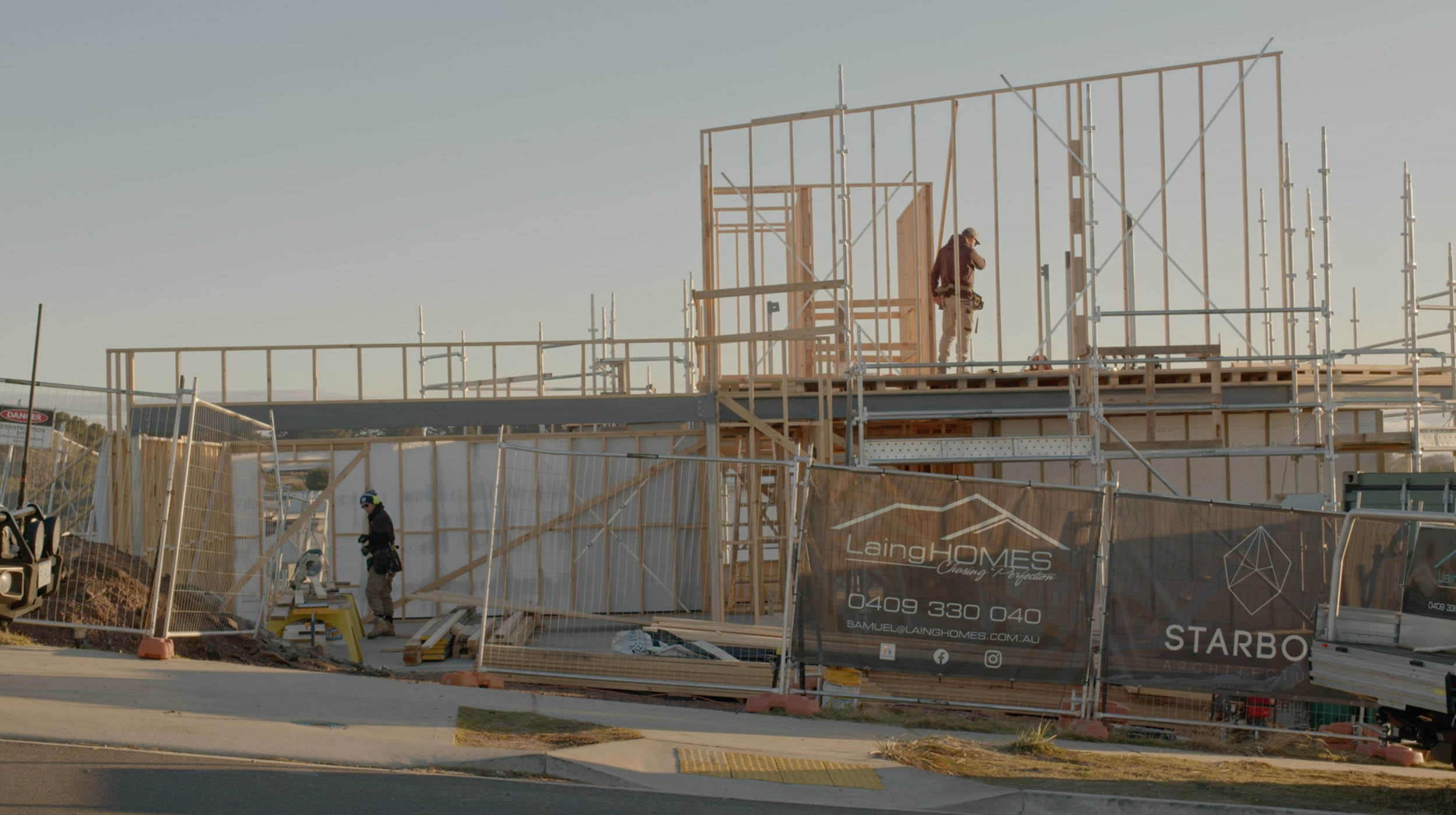 Two people on a construction site with a house frame.