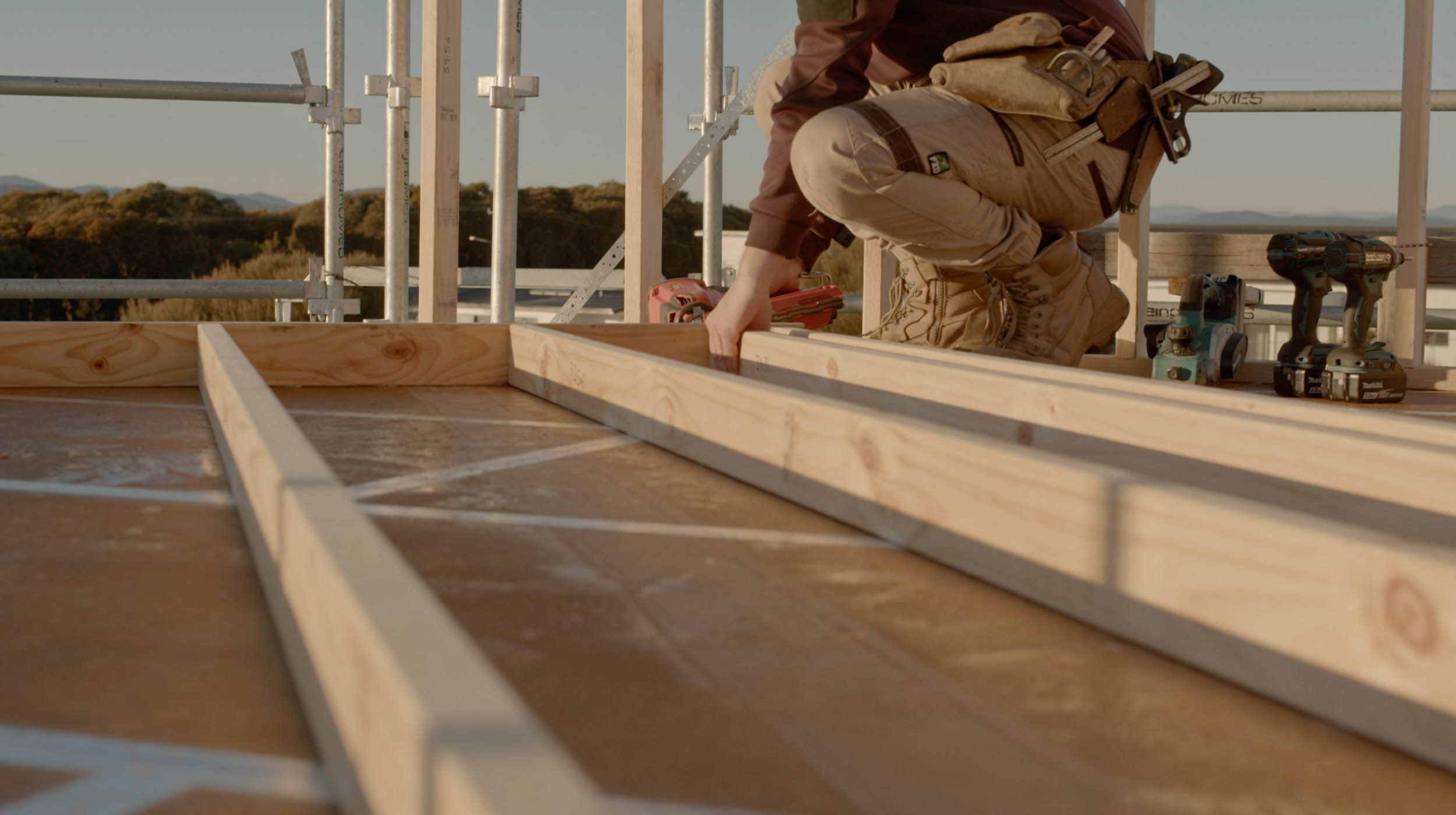 A person fitting some nails to a wooden house frame.