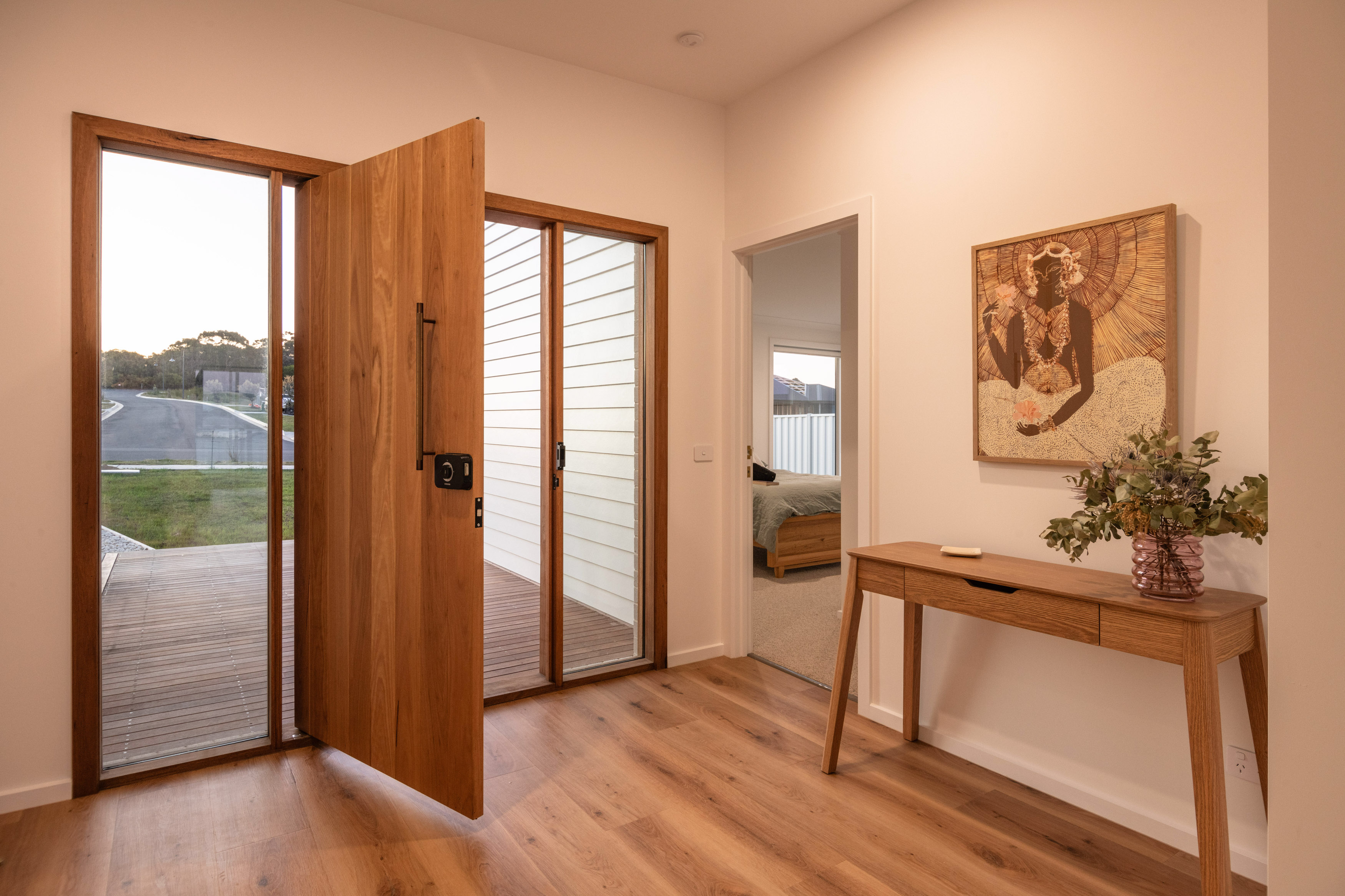 An Internal image of a doorway with a large orange wooden door and nice beige wooden table with polished floor boards.