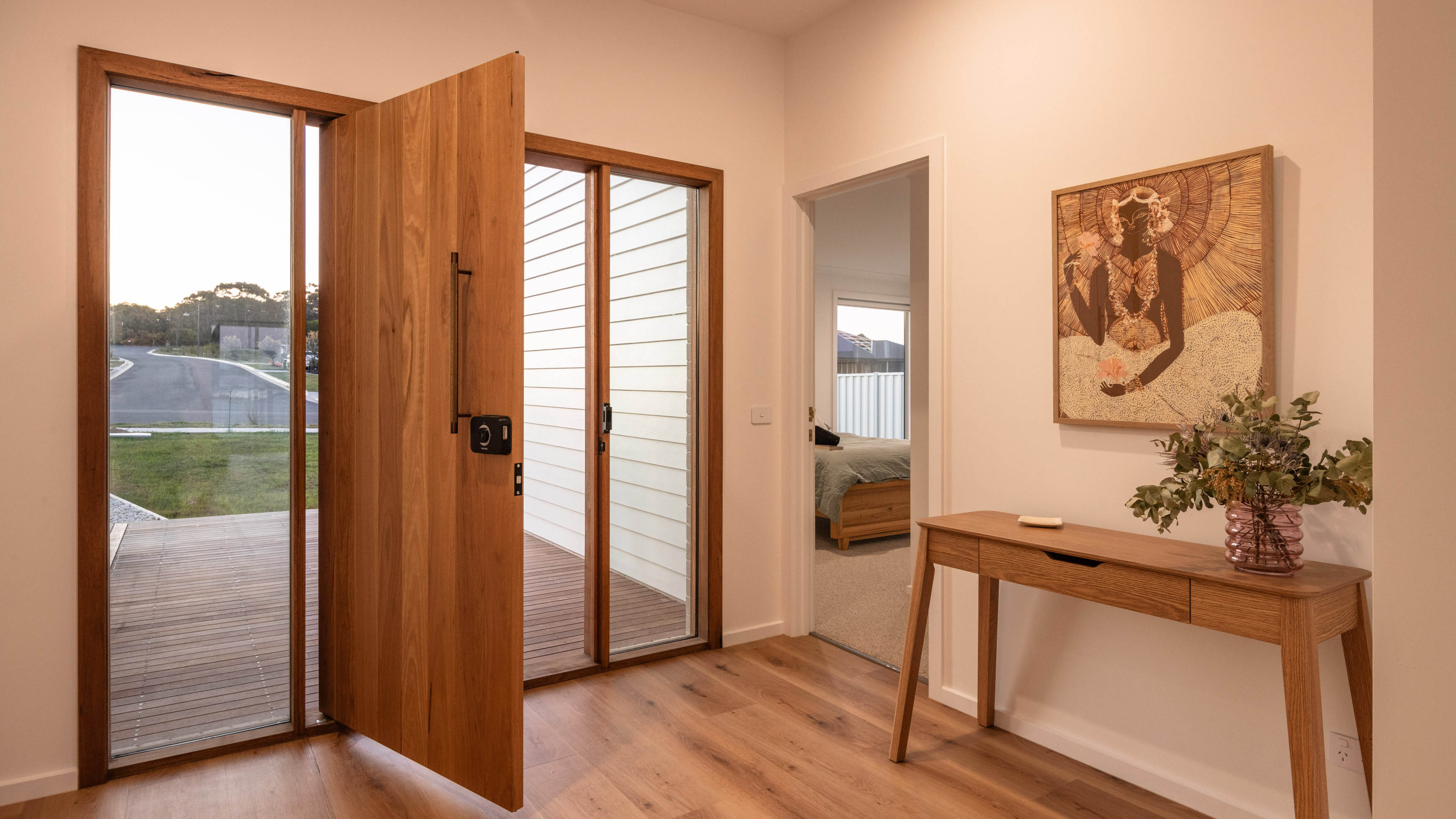 An Internal image of a doorway with a large orange wooden door and nice beige wooden table with polished floor boards.