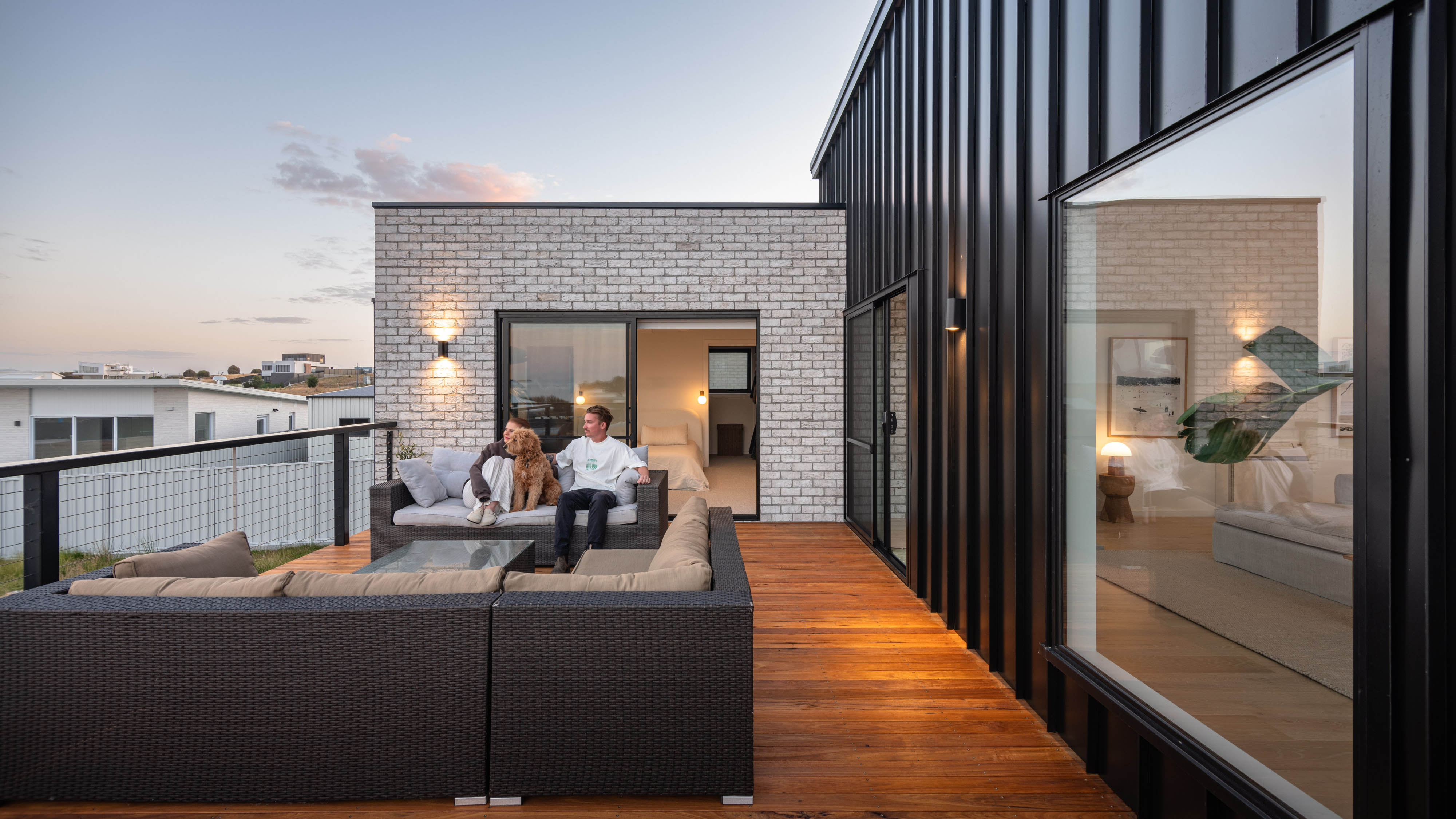A House with an orange wood deck with outdoor sofas sitting on it.