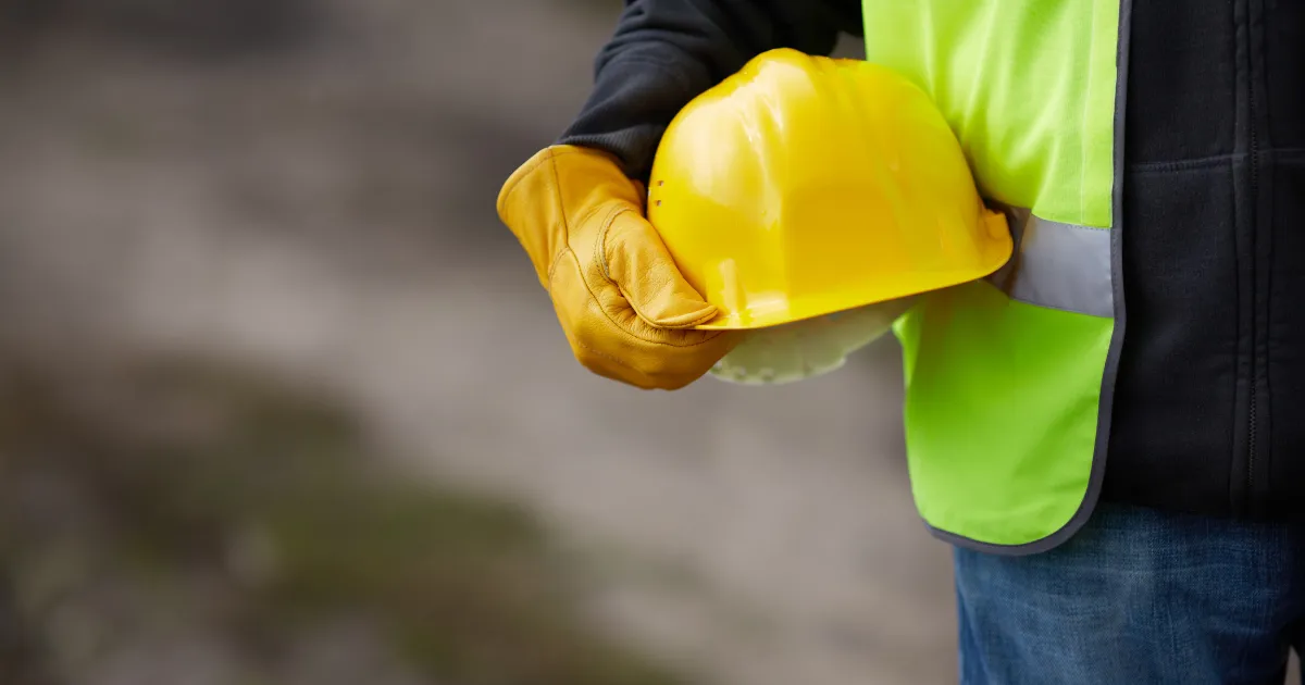 Hand of a construction worker holding a hard hat.