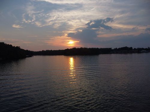 Sunset over a calm lake with silhouetted trees and a glowing reflection on the water.
