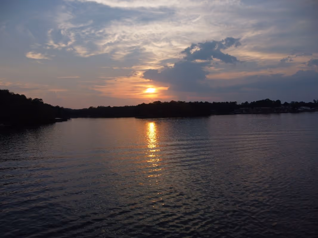 Sunset over a calm lake with silhouetted trees and a glowing reflection on the water.