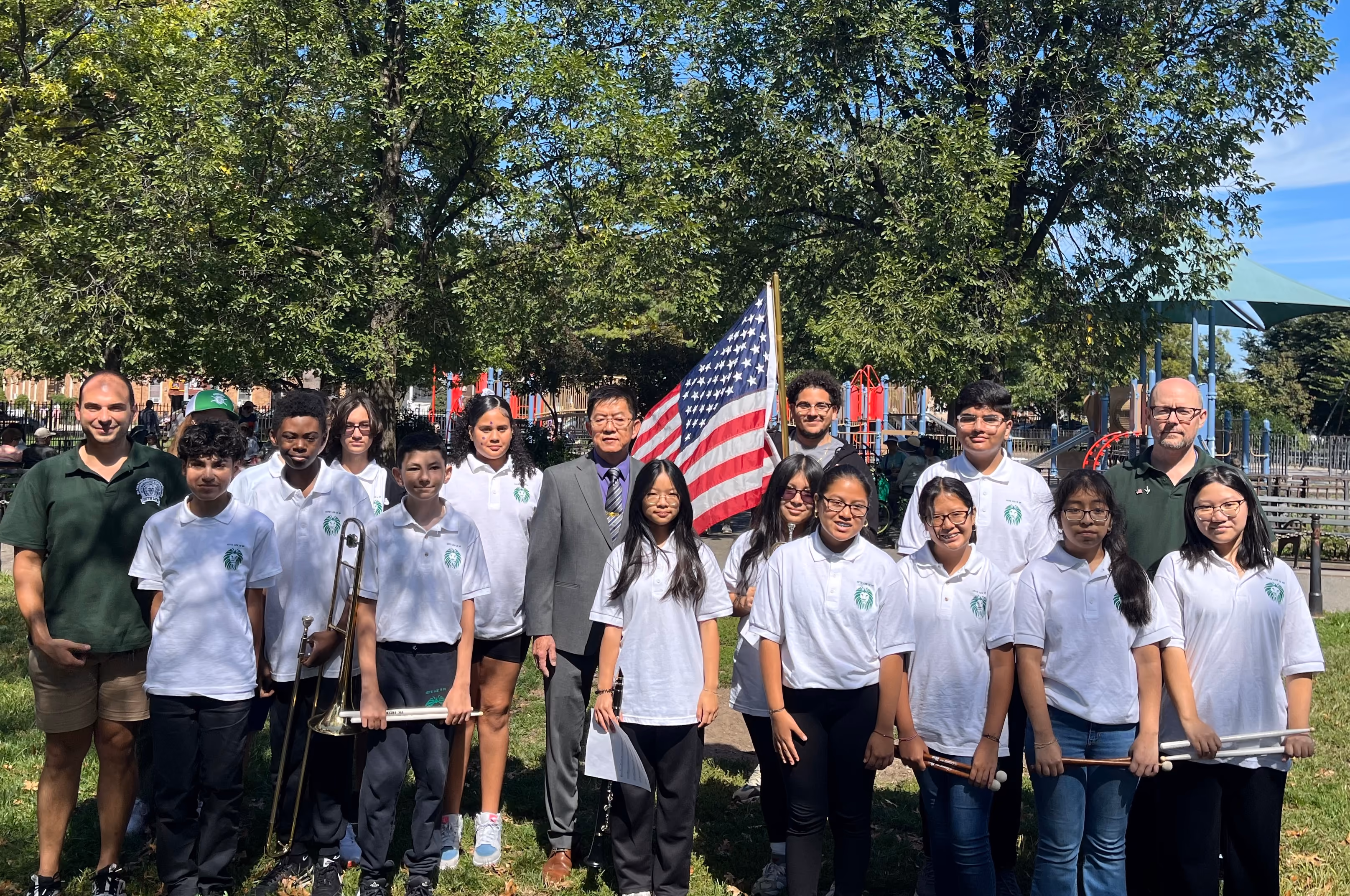 Student band members and staff pose outdoors with American flag