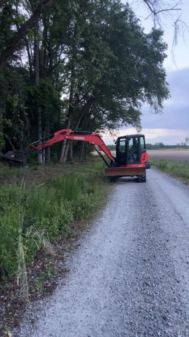 Red excavator parked on gravel road near trees and grassy field