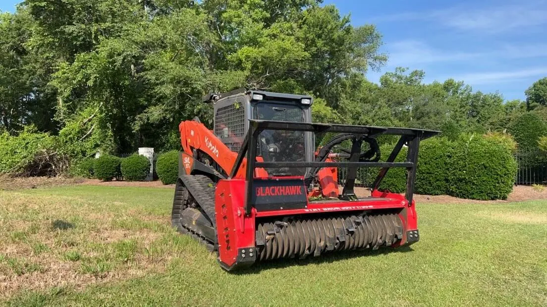 Red Blackhawk mulching machine on tracked wheels in landscaped yard