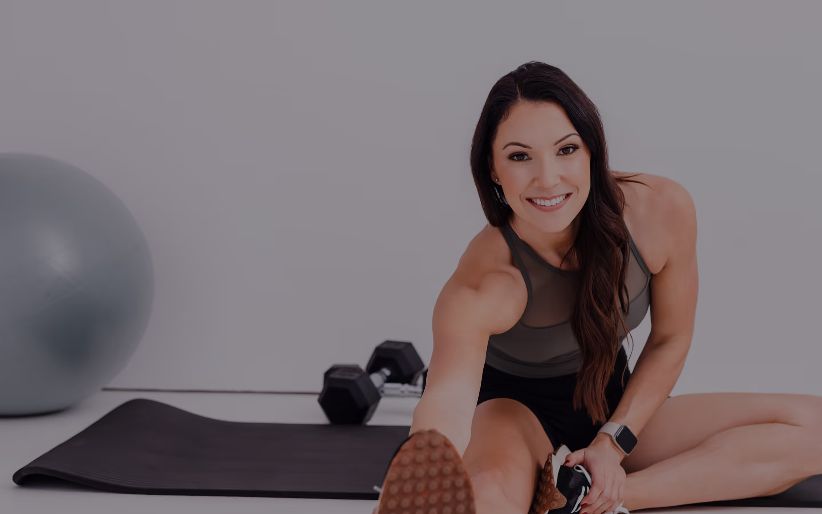 A woman sitting on a mat with a dumbbell.
