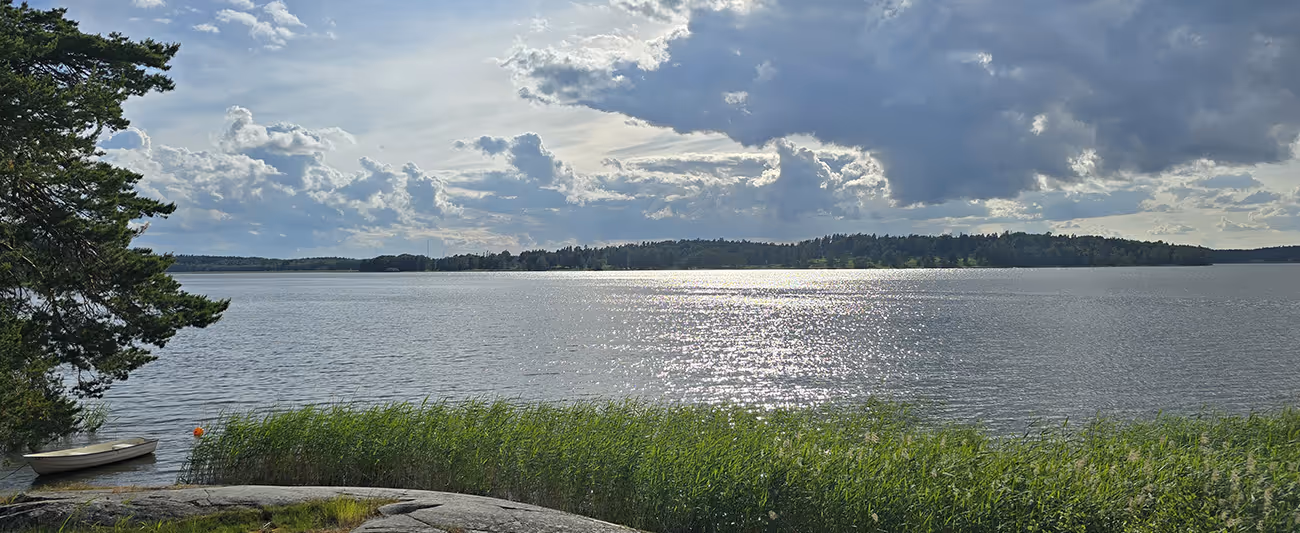 Lugn sjöutsikt med båt, vass och solreflektioner på vattenytan