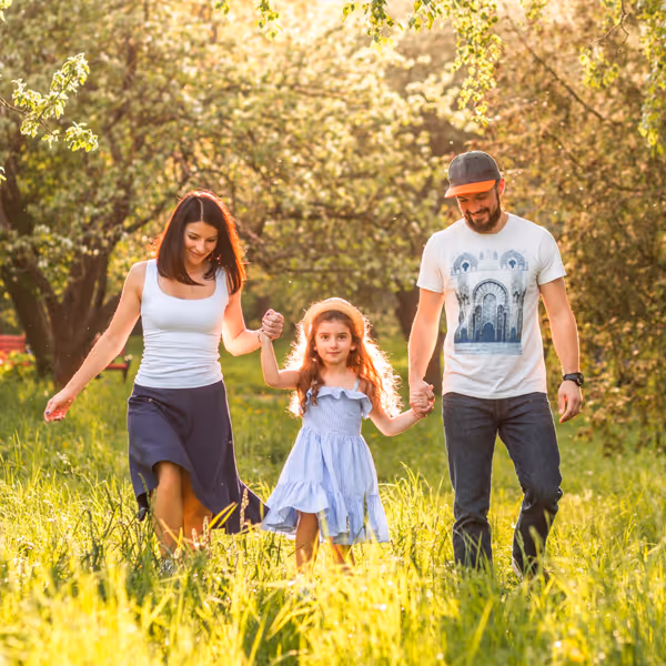 Familj som promenerar tillsammans i solig äng med gröna träd