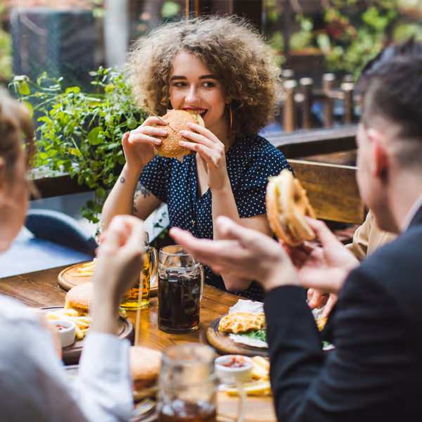 Lockig kvinna äter hamburgare med vänner på restaurang