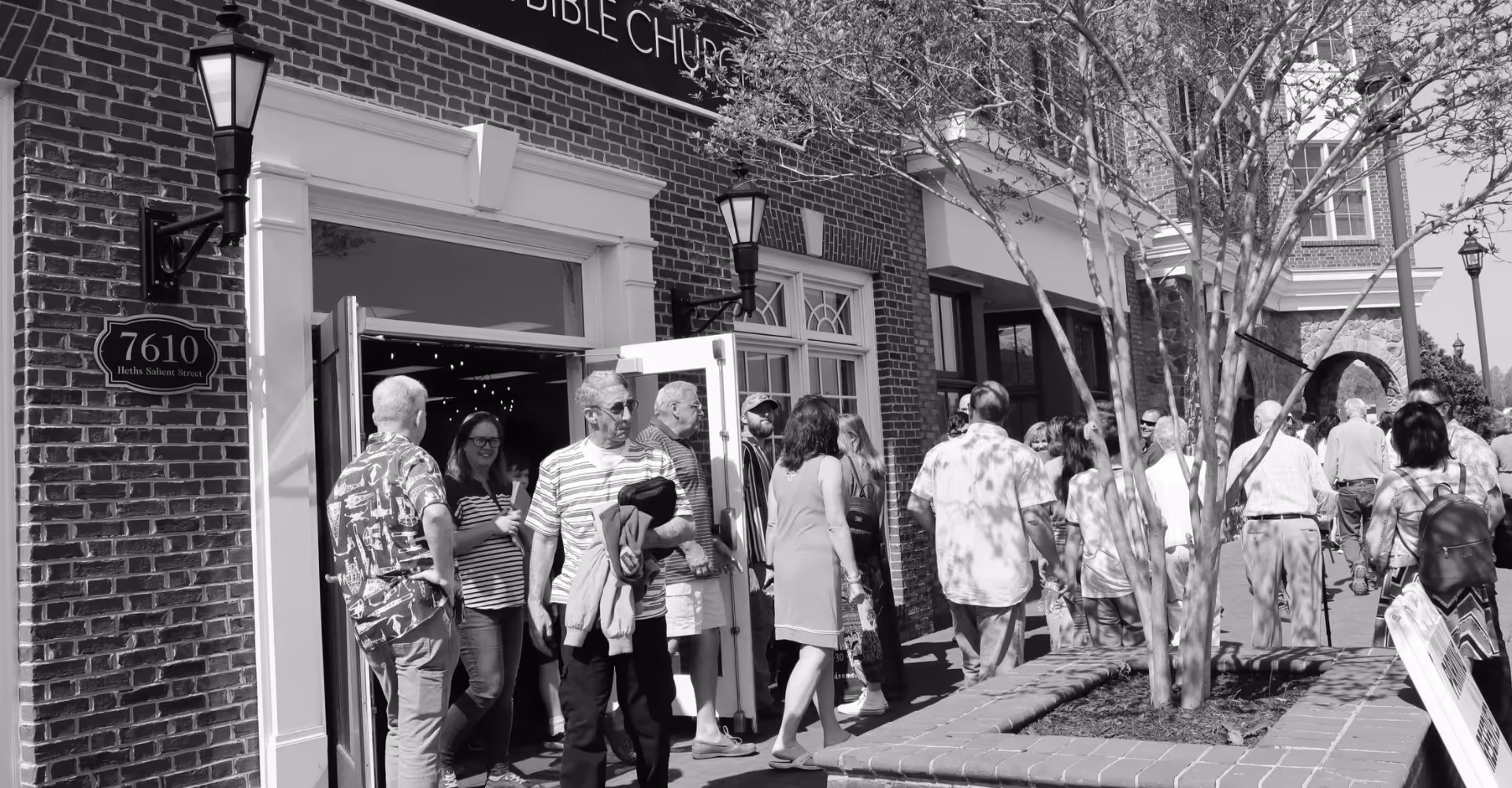 Group of people gathered outside the entrance of a brick building with a sign showing the address 7610 Heths Salient Street.