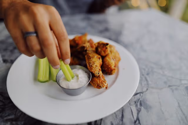 A person holding a celery stalk with a white plate of food.
