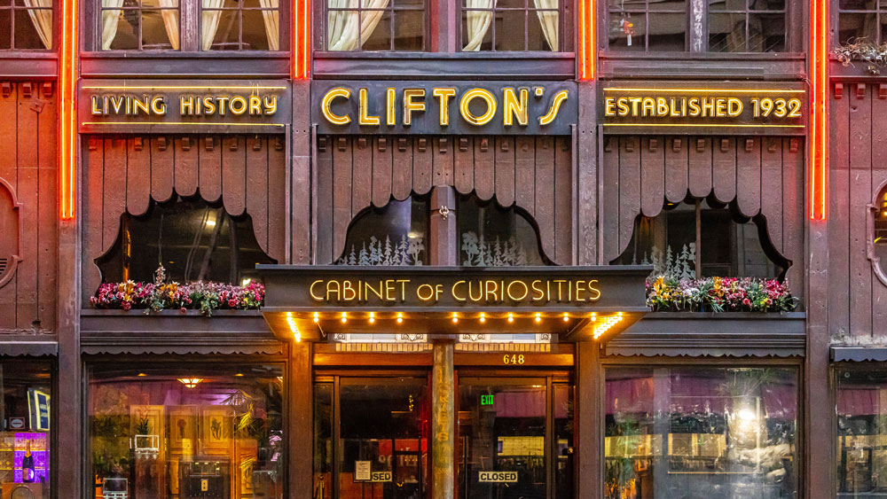Facade of Clifton's Cabinet of Curiosities with neon signs saying Living History, Established 1932, and a flower-adorned entrance.