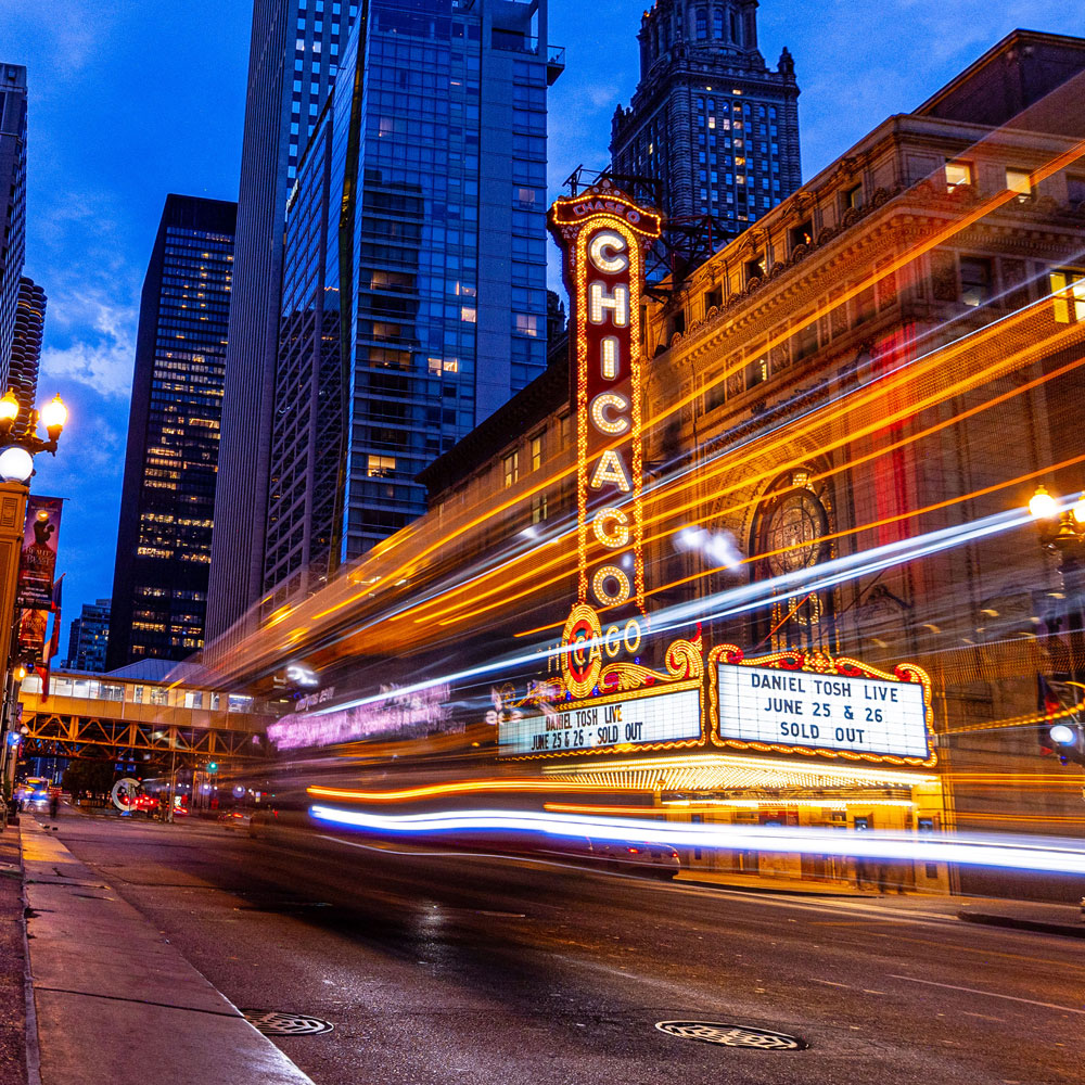 Chicago Theatre bright marquee and vertical sign at dusk with light trails from moving vehicles on the street.
