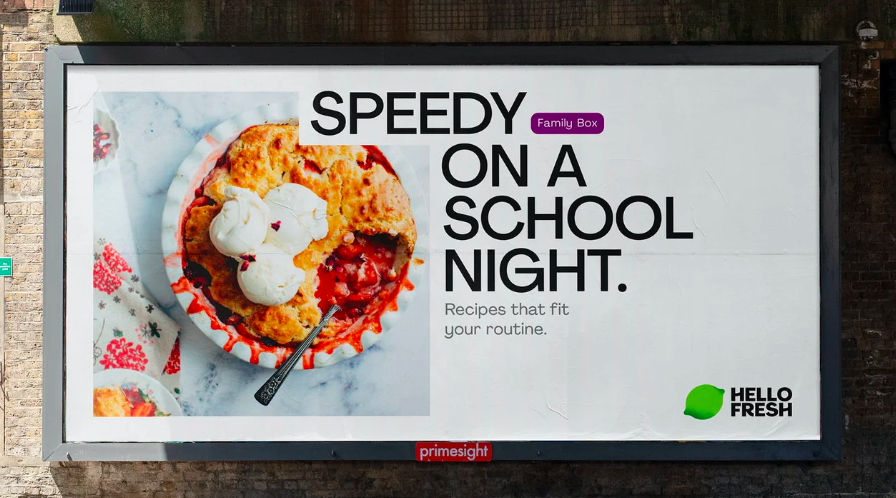 Billboard advertisement for hello fresh's "family box," featuring an image of a prepared meal with the tagline "speedy on a school night" against a brick wall background.