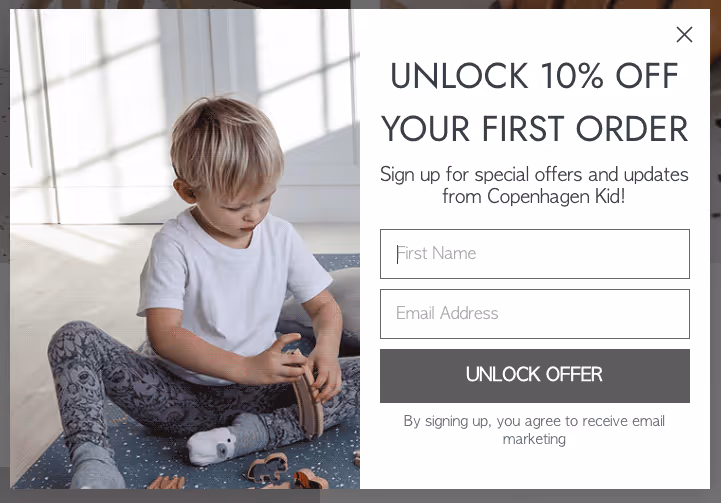 A young child in a white shirt and patterned pants sits on a blue carpet, playing with wooden toys. A lead generation form on the right offers 10% off for signing up with a name and email, featuring a button labeled "Unlock Offer.