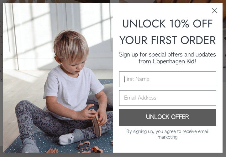 A young child in a white shirt and patterned pants sits on a blue carpet, playing with wooden toys. A lead generation form on the right offers 10% off for signing up with a name and email, featuring a button labeled "Unlock Offer.