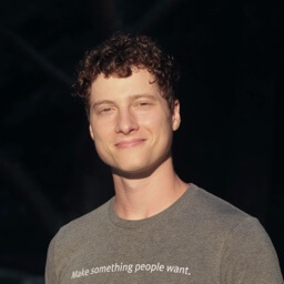 Smiling young man with curly hair wearing a gray shirt that says 'Make something people want.'
